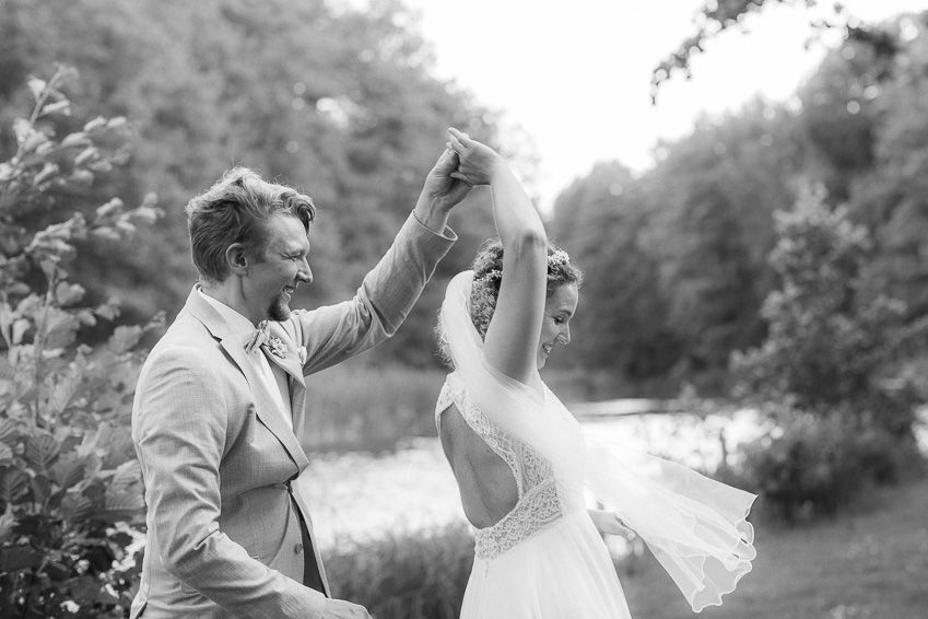 Groom twirls bride in flowing veil outdoors in black and white wedding photo.