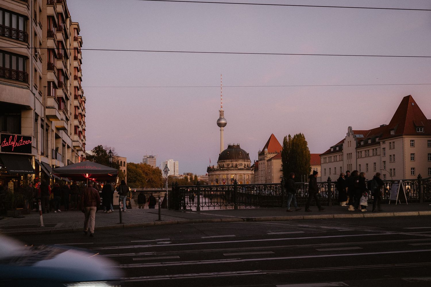 Berlin cityscape at dusk featuring the iconic TV tower and historic buildings along a busy street.