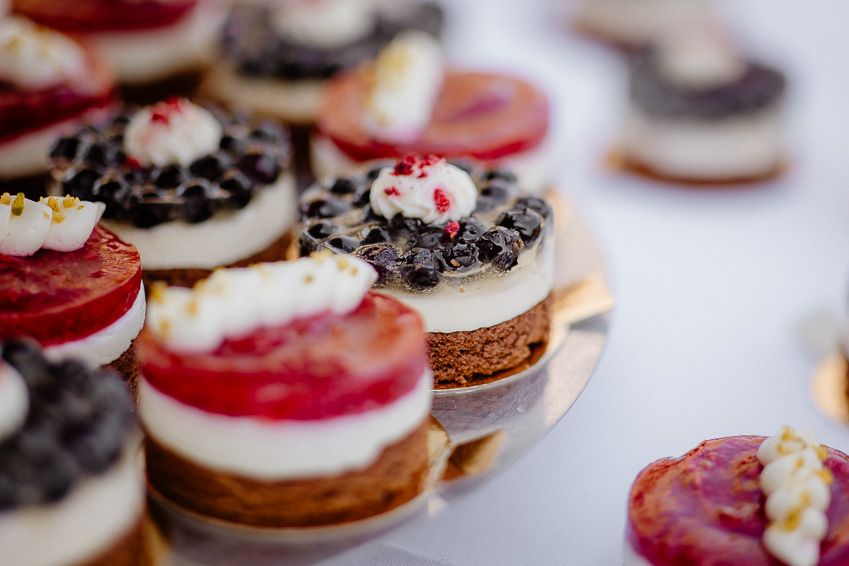 Elegant assorted mini cheesecakes topped with fresh strawberries, blueberries, and cream at a wedding dessert table.