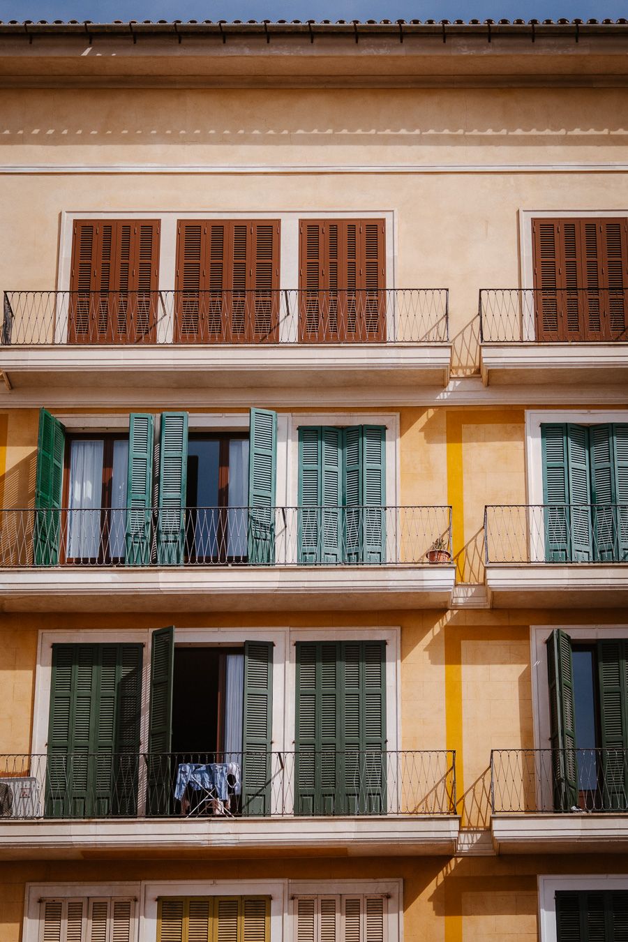 Colorful Mediterranean building facade with green and brown shuttered balconies in warm sunlight.