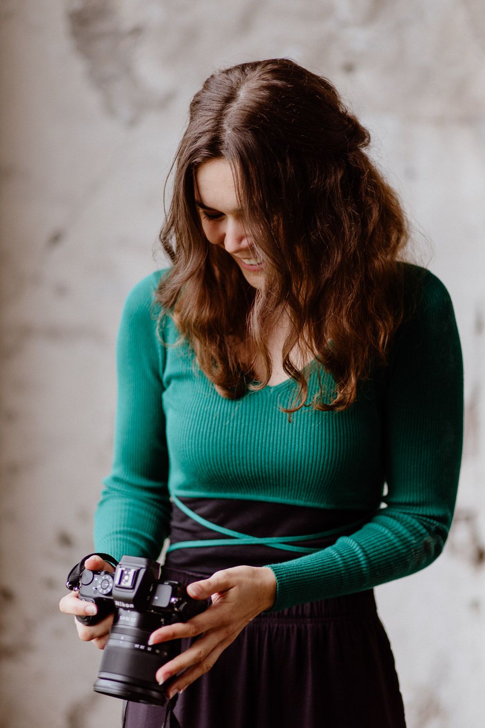 Brunette woman in green sweater reviewing photos on a camera indoors.