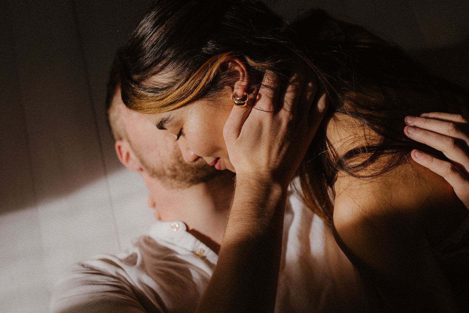 Intimate close-up of a couple sharing a tender kiss in soft natural window light.