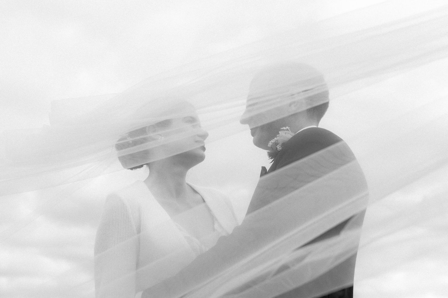 Romantic black and white double exposure portrait of bride and groom facing each other beneath flowing veil.