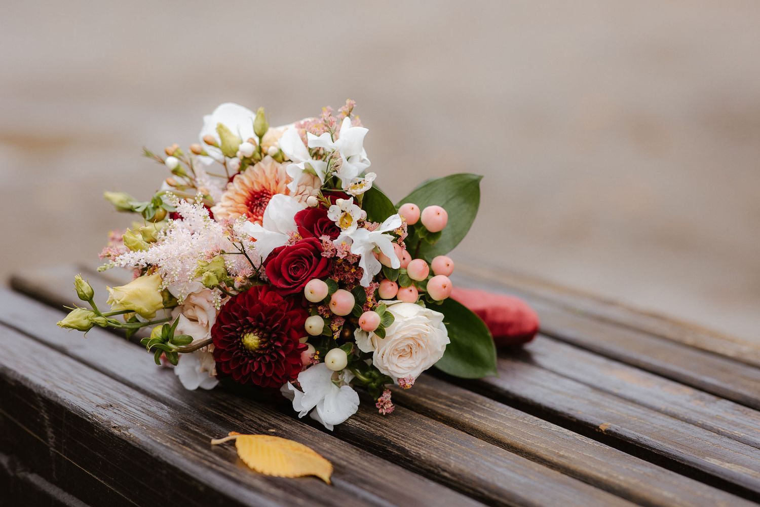 Bridal bouquet with red dahlias, white roses, and pink blooms resting on a wooden bench.