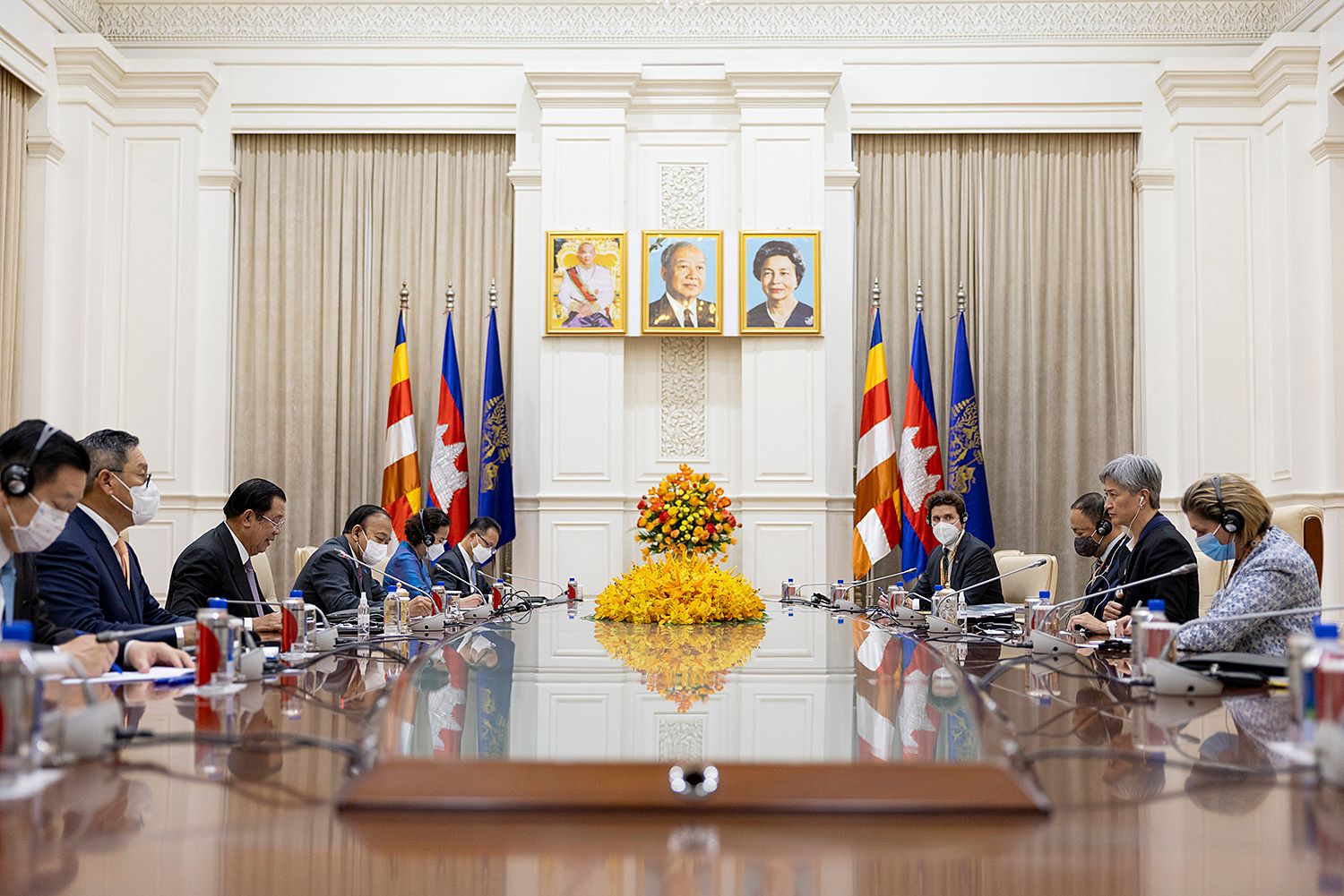 Diplomatic meeting at a conference table in Phnom Penh with flags and portraits, government officials seated on both sides in formal attire.
