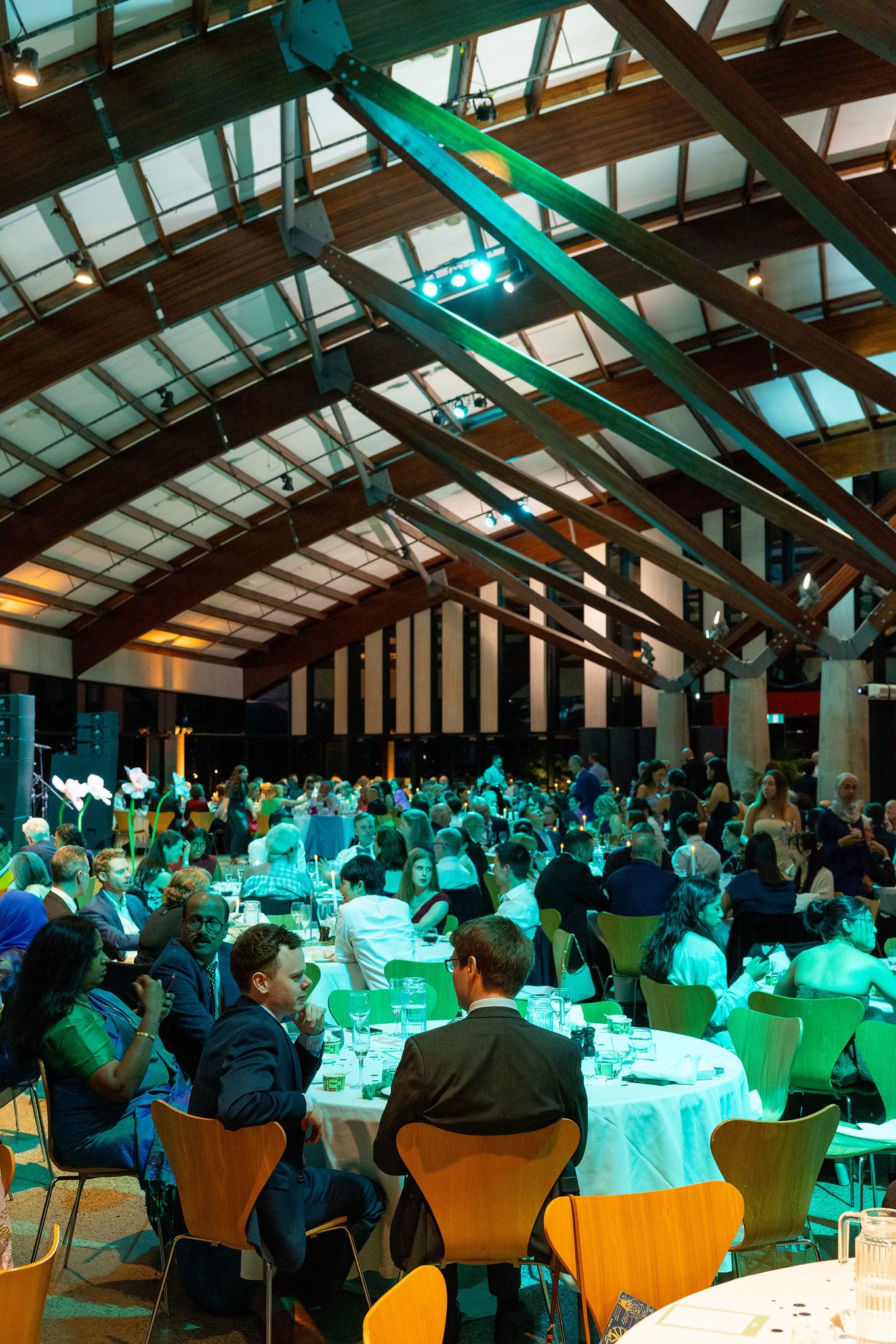 Large banquet hall filled with guests seated at round tables during a formal gala dinner event with green ambient lighting
