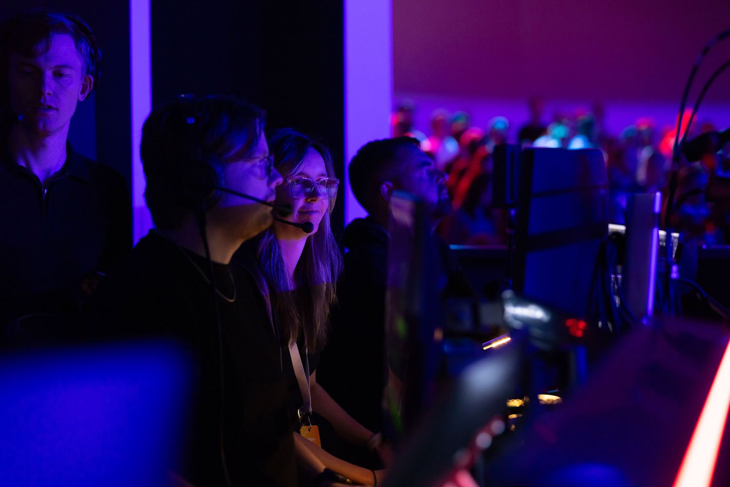 Event technical staff wearing headsets, glowing monitors in a dark, neon-lit music event.