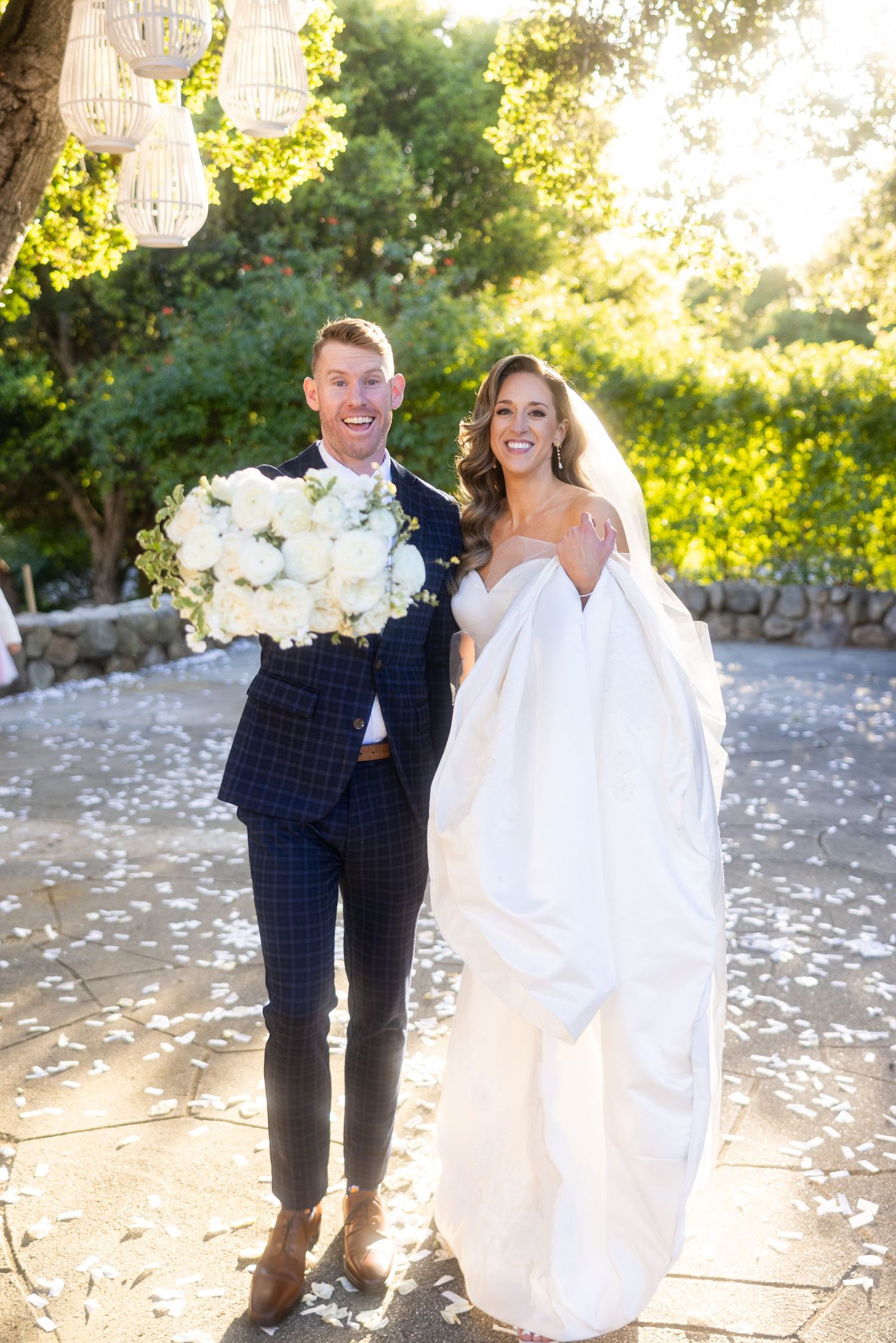 A happy couple shares a joyful moment on their wedding day in a sunlit garden with hanging crystal chandeliers.