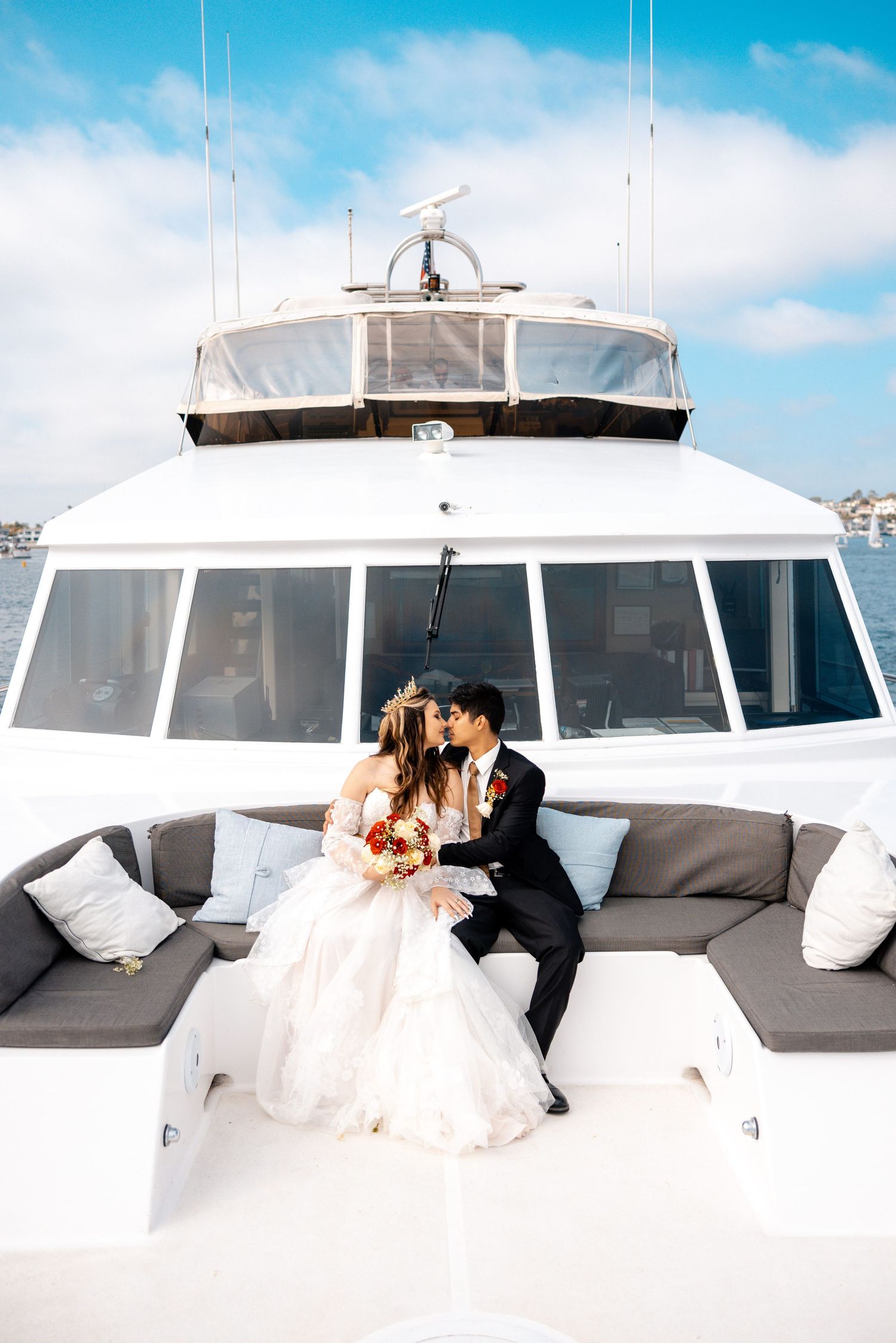 A couple enjoys an intimate moment on the deck of a luxury yacht under bright blue skies.