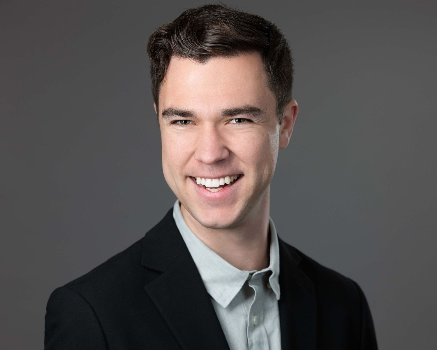 Professional headshot of a person in business attire against a gray background.