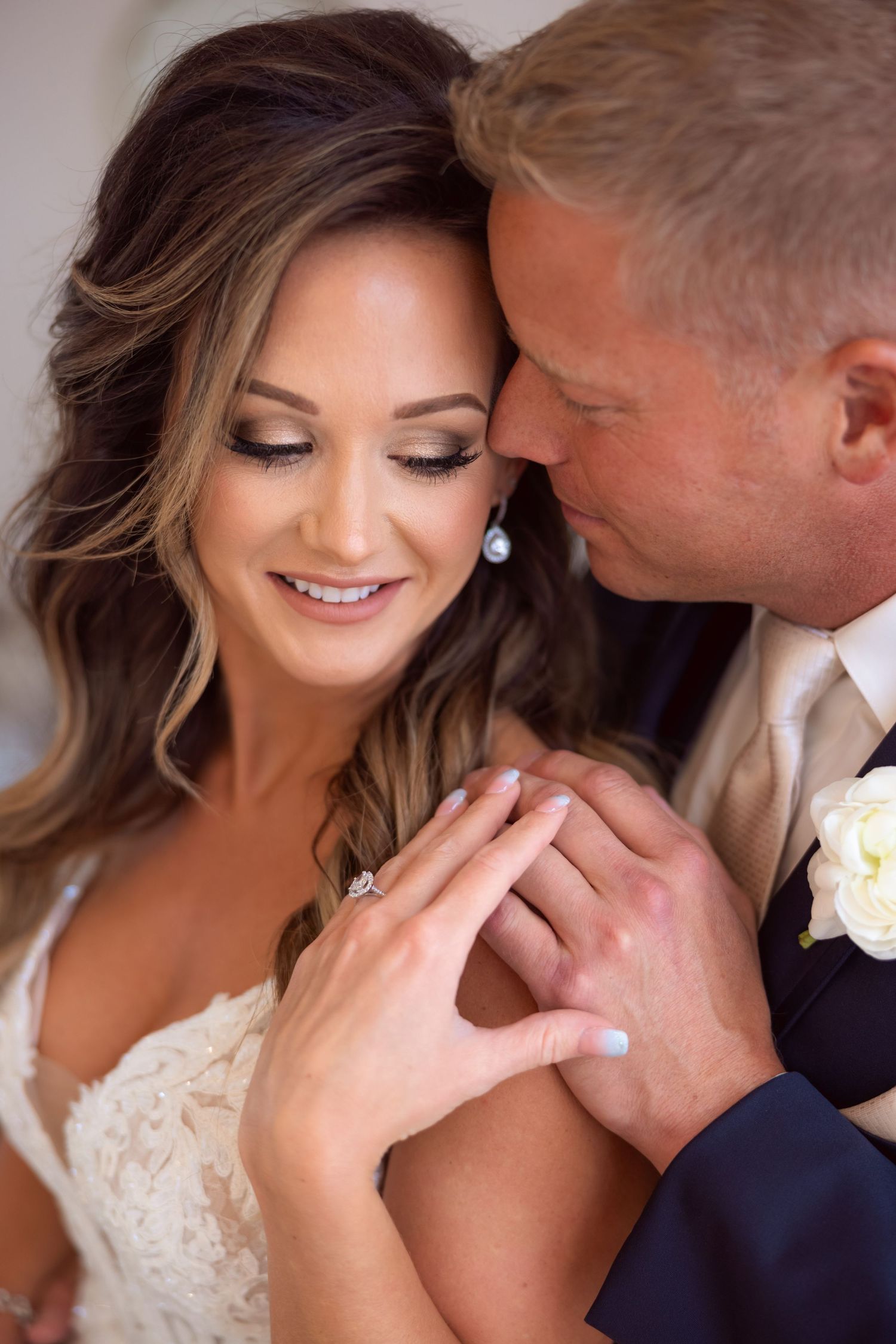 Close up wedding photo of a tender moment between newlyweds with bride in lace dress showing joyful smile and styled hair.