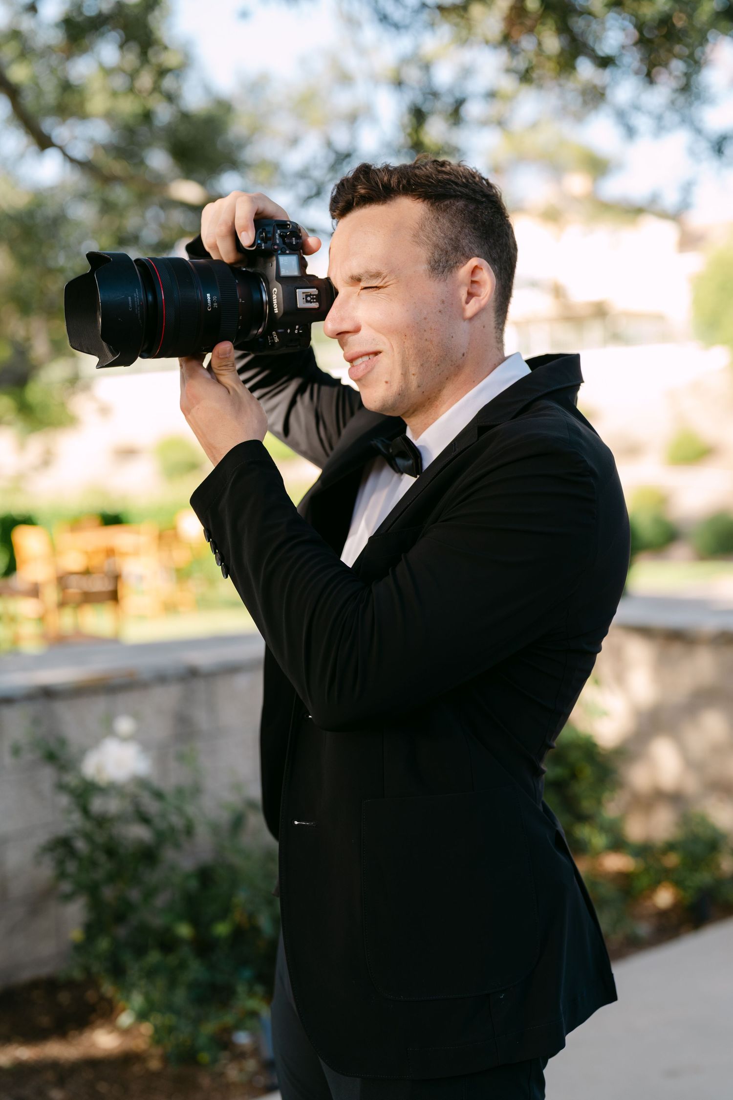 Professional photographer in black jacket uses telephoto lens to capture shots during outdoor photo session.