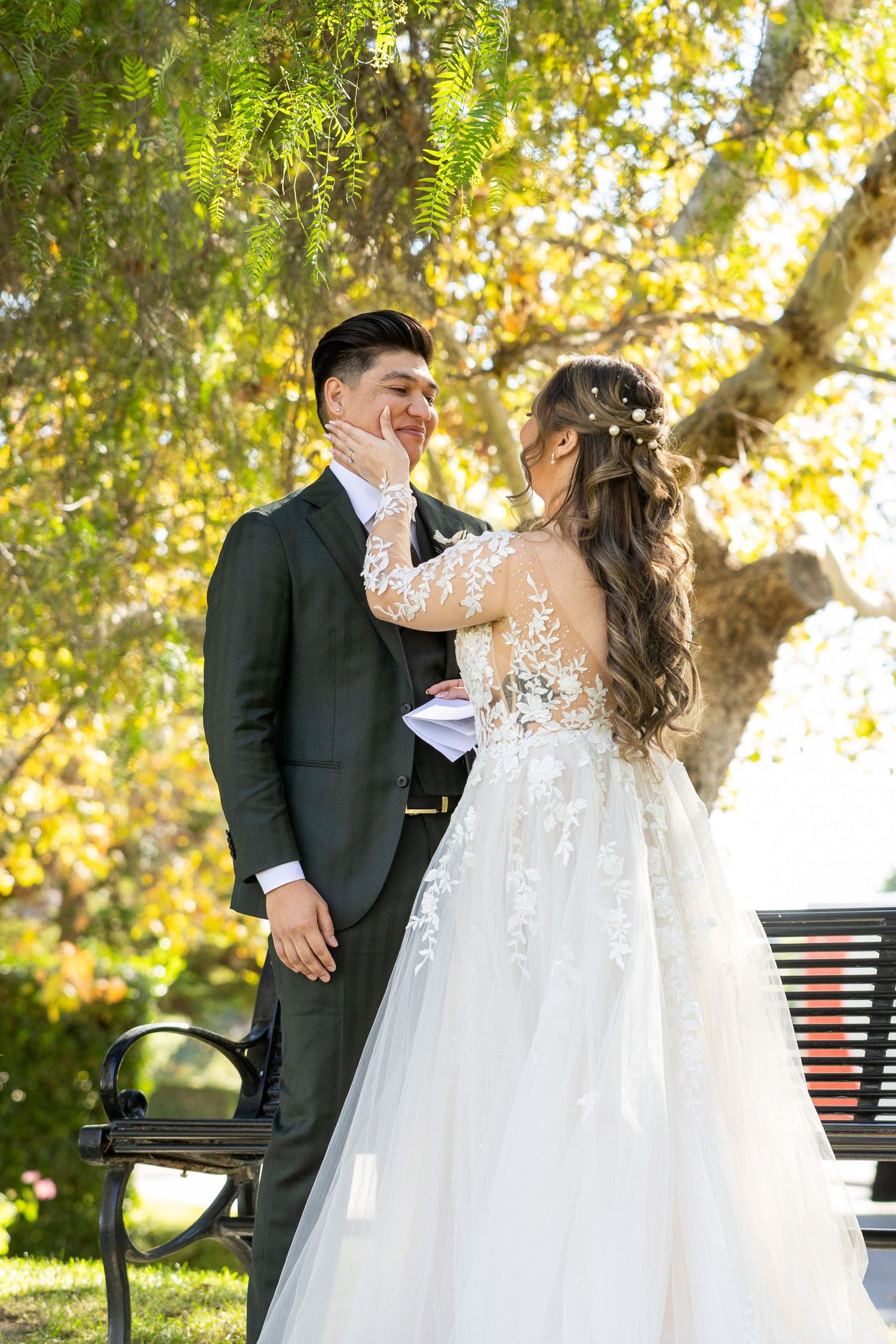 Newlywed couple shares a joyful moment together in a garden setting with autumn foliage and sunlight filtering through trees.