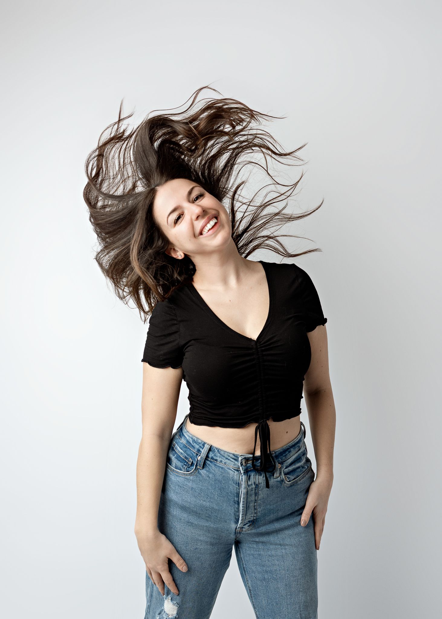 Dynamic fashion sequence showing model in black crop top and jeans doing energetic spinning dance movements against gray background.