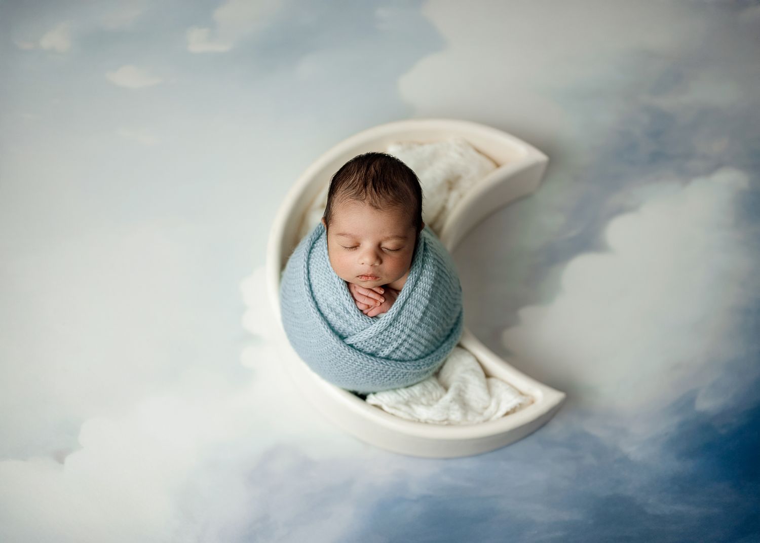 Dreamy cloud-themed newborn photography backdrop with soft blue and white colors creates ethereal atmosphere.