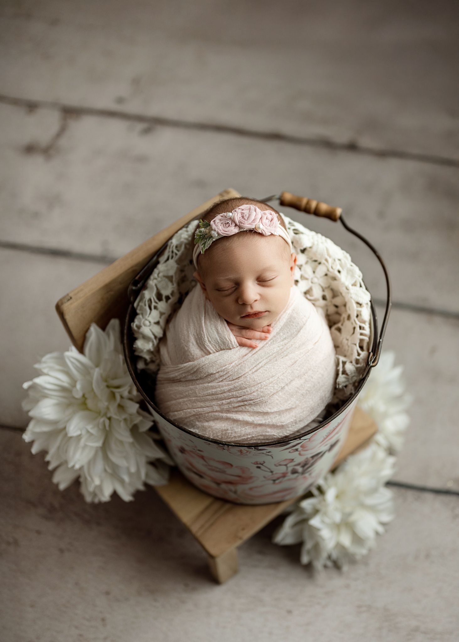 A series of newborn photography shots showing a sleeping baby wrapped in cream fabric with white flowers in a wooden bowl.