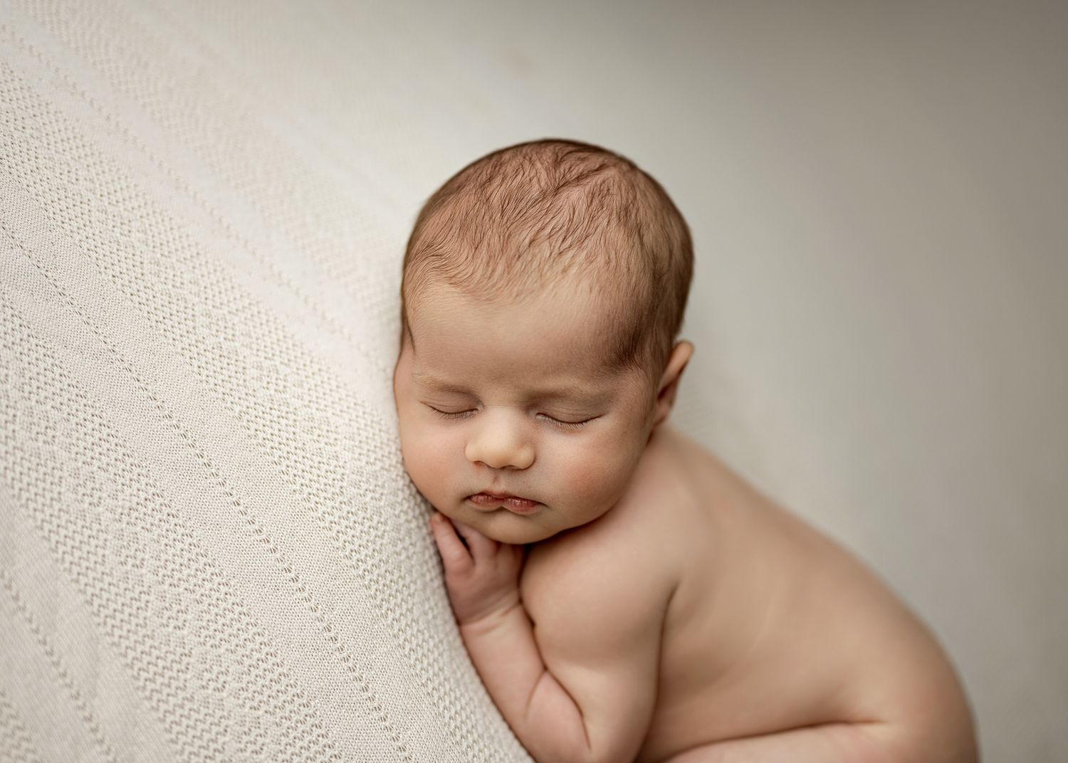 Serene newborn resting on textured cream blanket in gentle studio lighting.