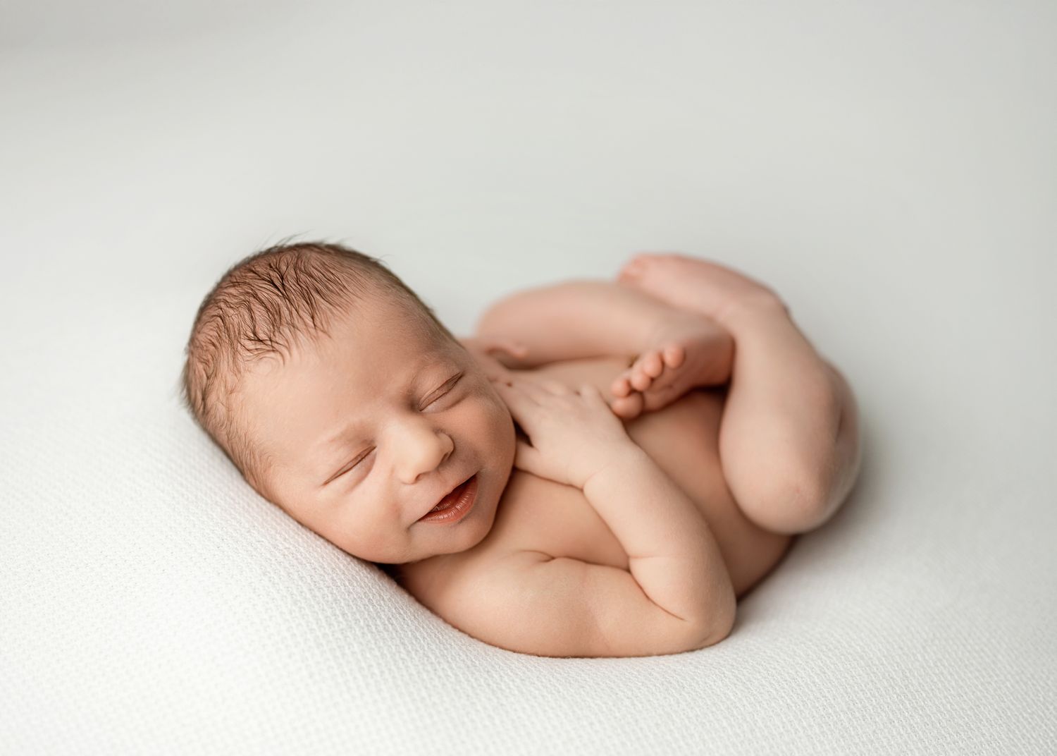 A sleeping newborn baby lies peacefully on soft white fabric in a minimalist photography composition.