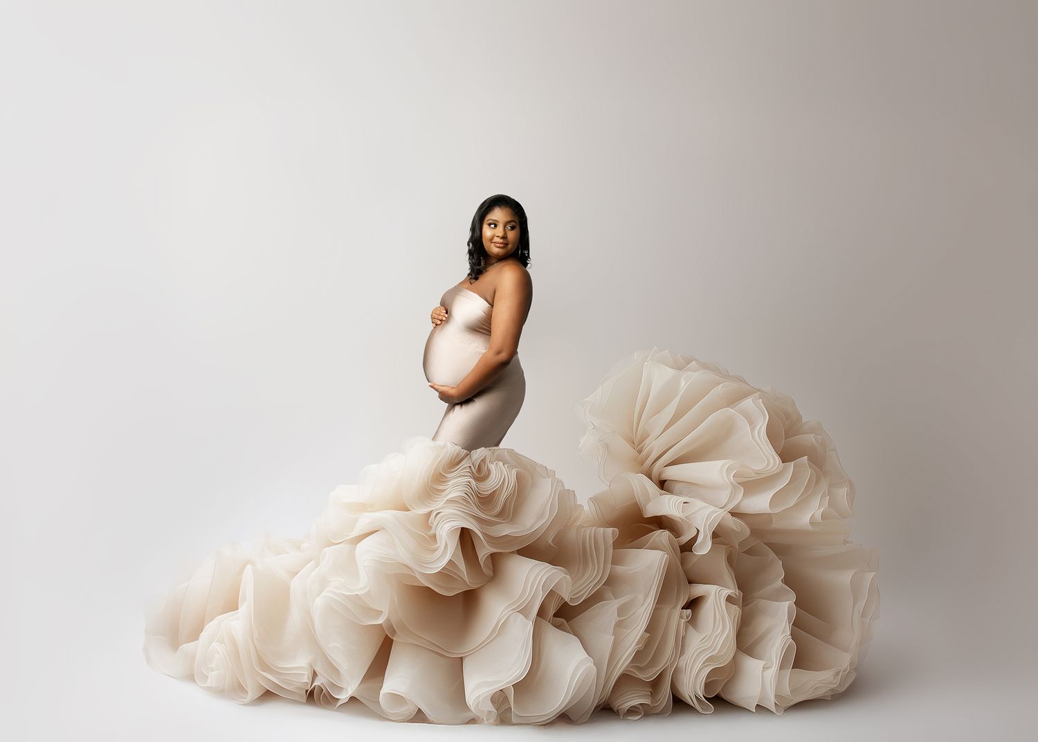 A nude maternity silhouette portrait featuring a cream-colored flowy tulle skirt arrangement against a grey background.