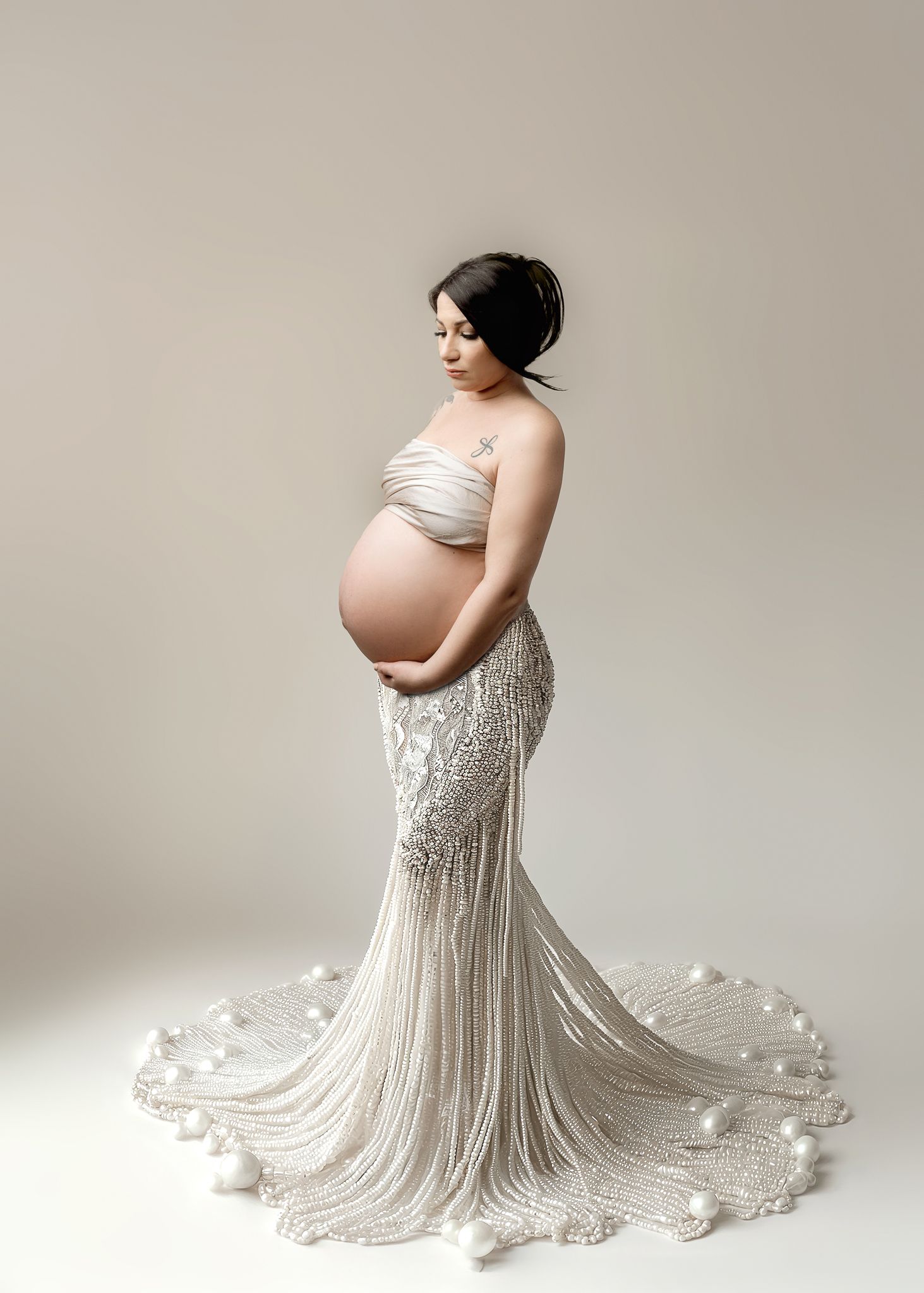 Elegant maternity photo featuring a white lace gown with long train against a neutral backdrop.