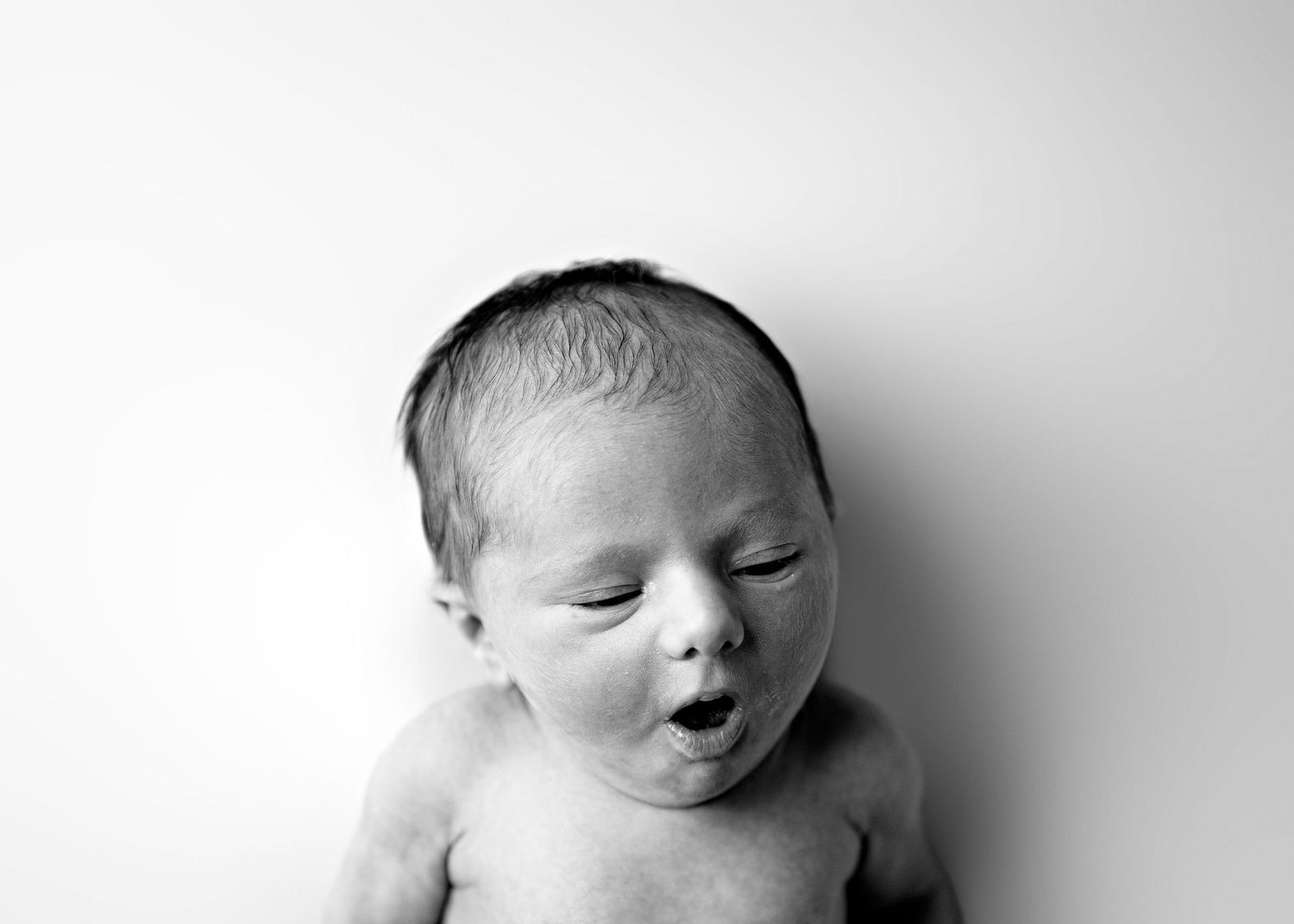 Black and white portrait of a newborn baby with closed eyes and expressive facial features against a light background.