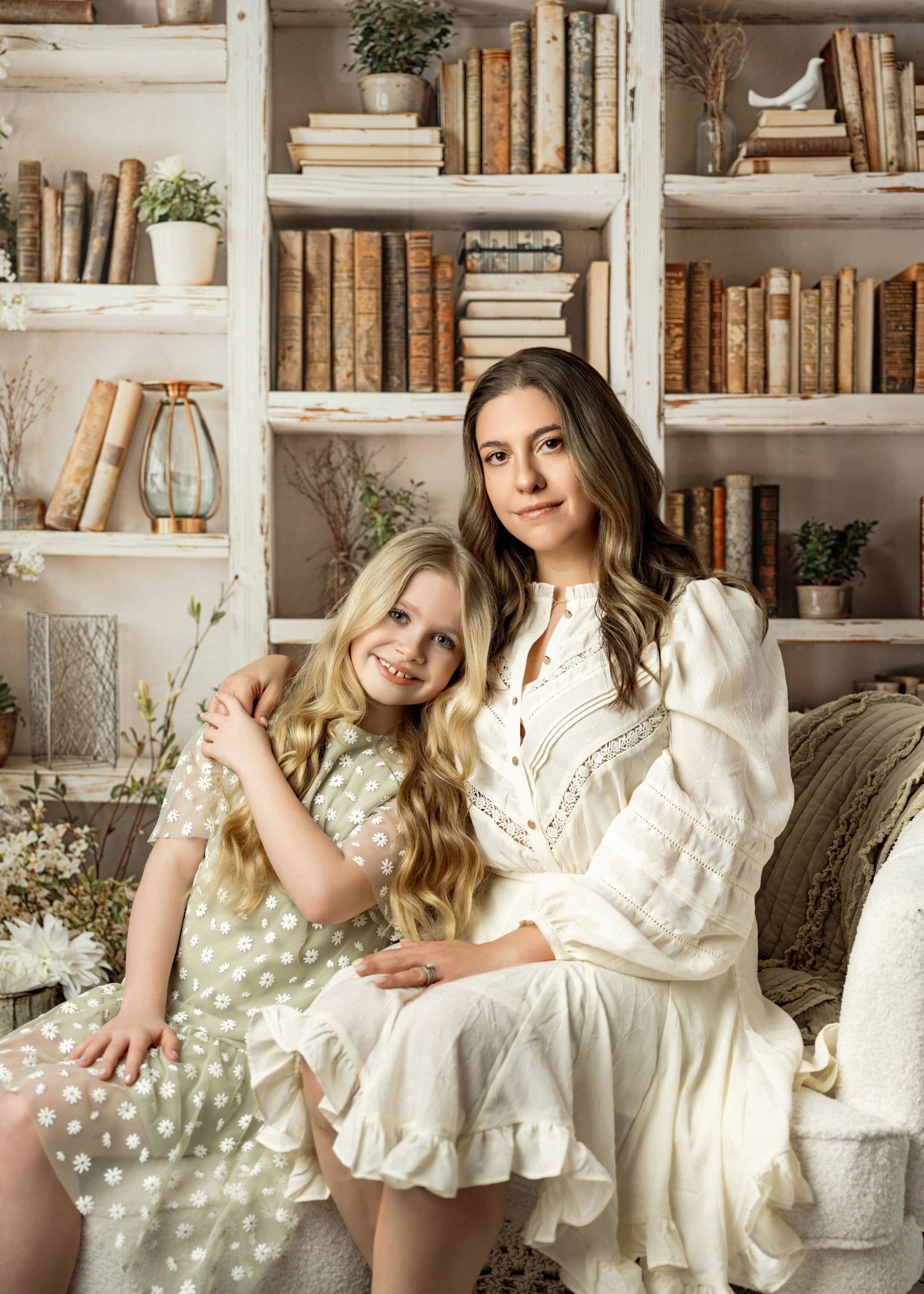 A vintage-inspired portrait in front of white bookshelves filled with antique books and small potted plants.