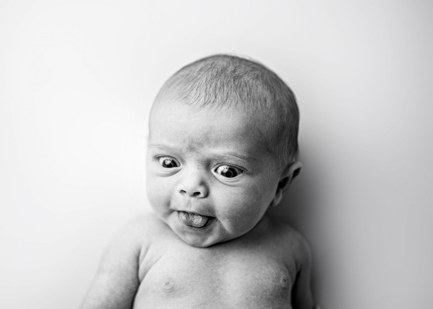 Black and white portrait of a baby with an expressive smile against a light background.