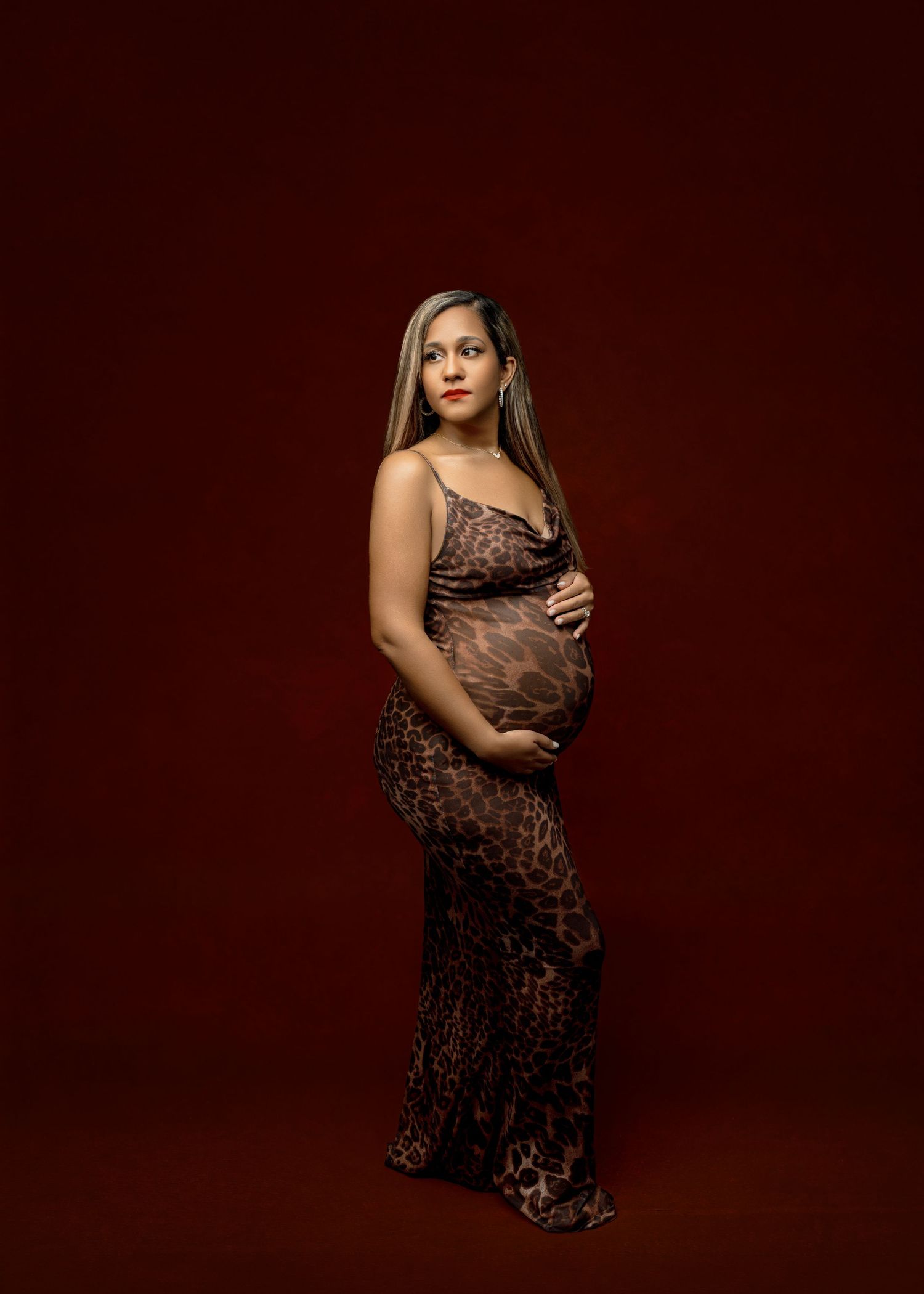 A maternity photo shows an expectant mother in a lace dress posing against a deep burgundy background.