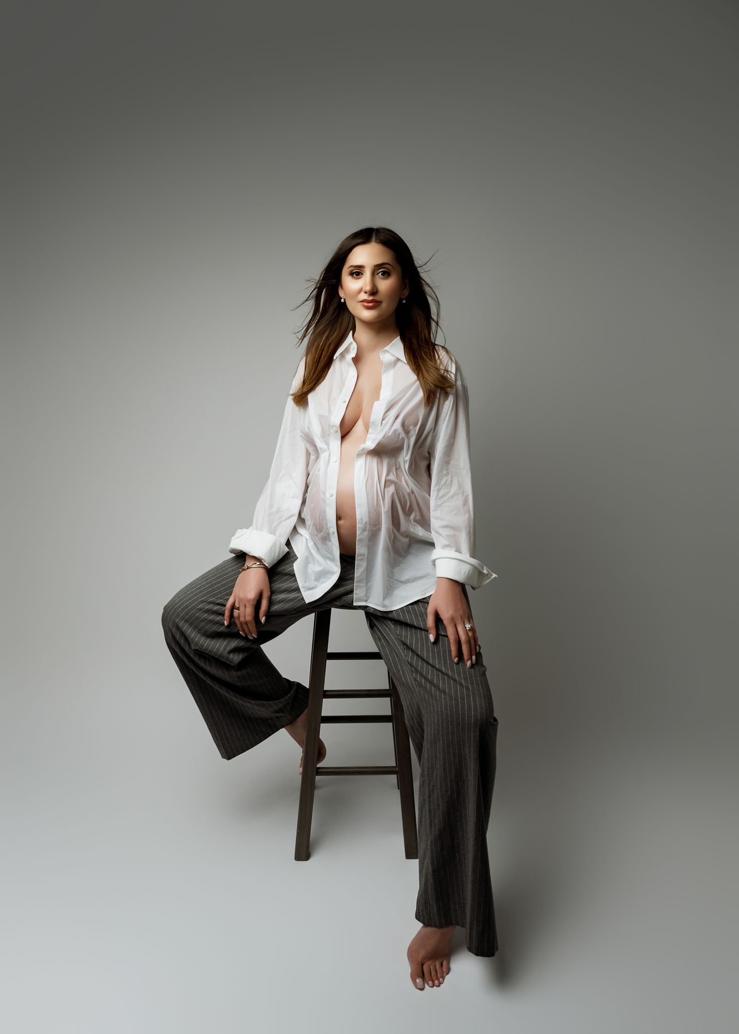 Professional studio portrait series showing figure in white button-down shirt and gray pants posing on wooden chair.