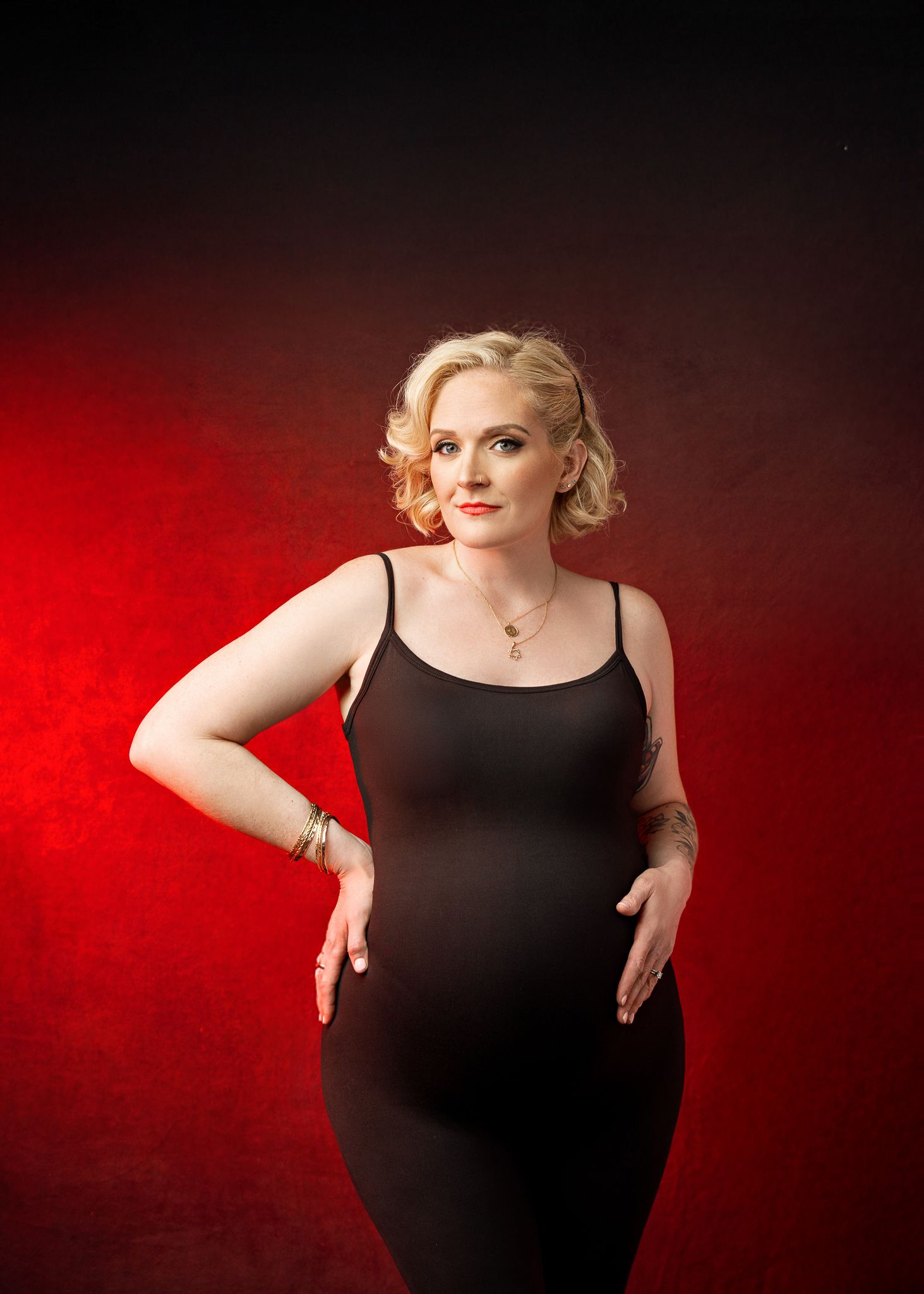 Studio portrait of a person in a black dress posing elegantly against a dramatic red gradient background.