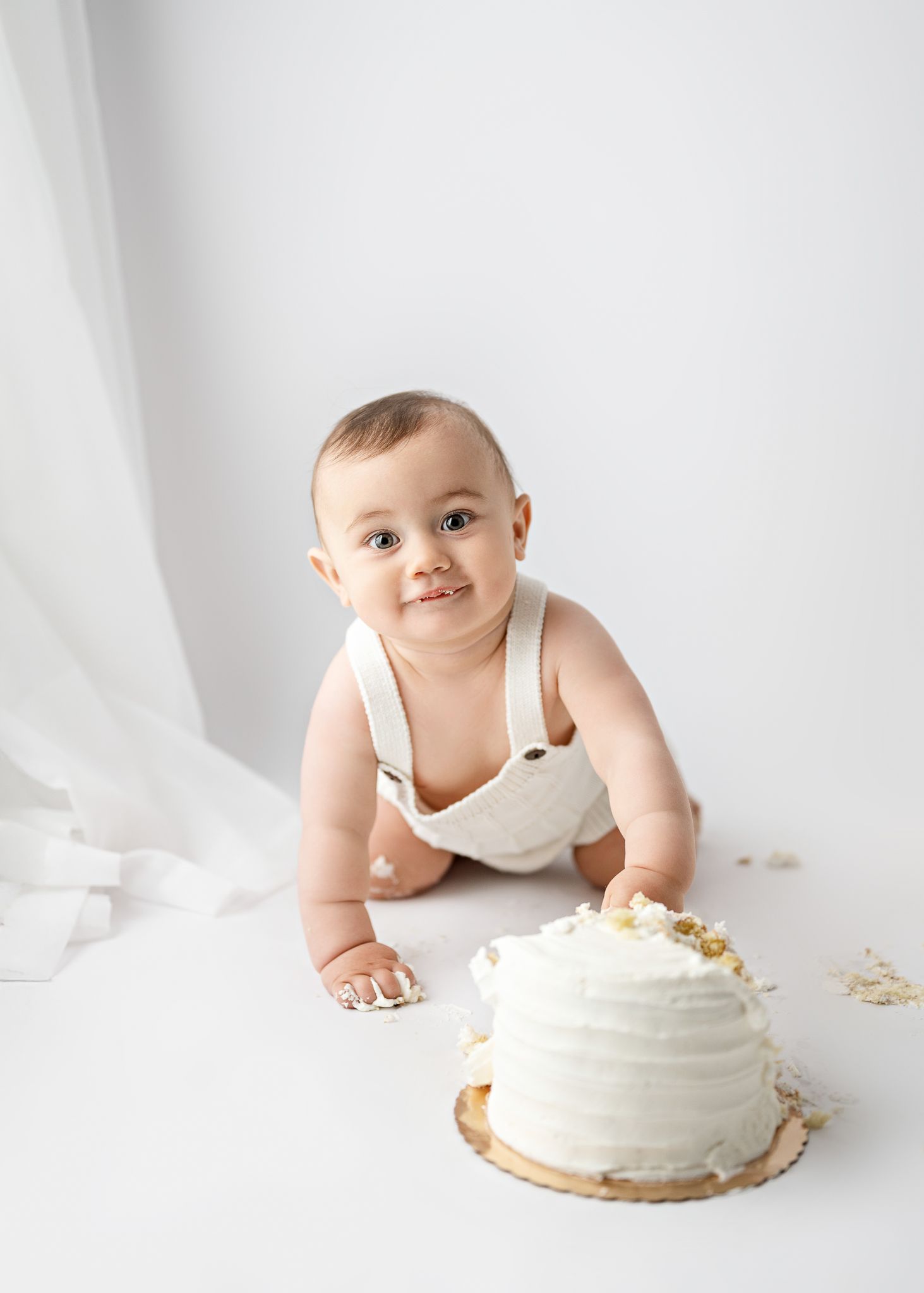 Baby in white outfit crawling and smashing frosted cake in progressive sequence of milestone first birthday photos.
