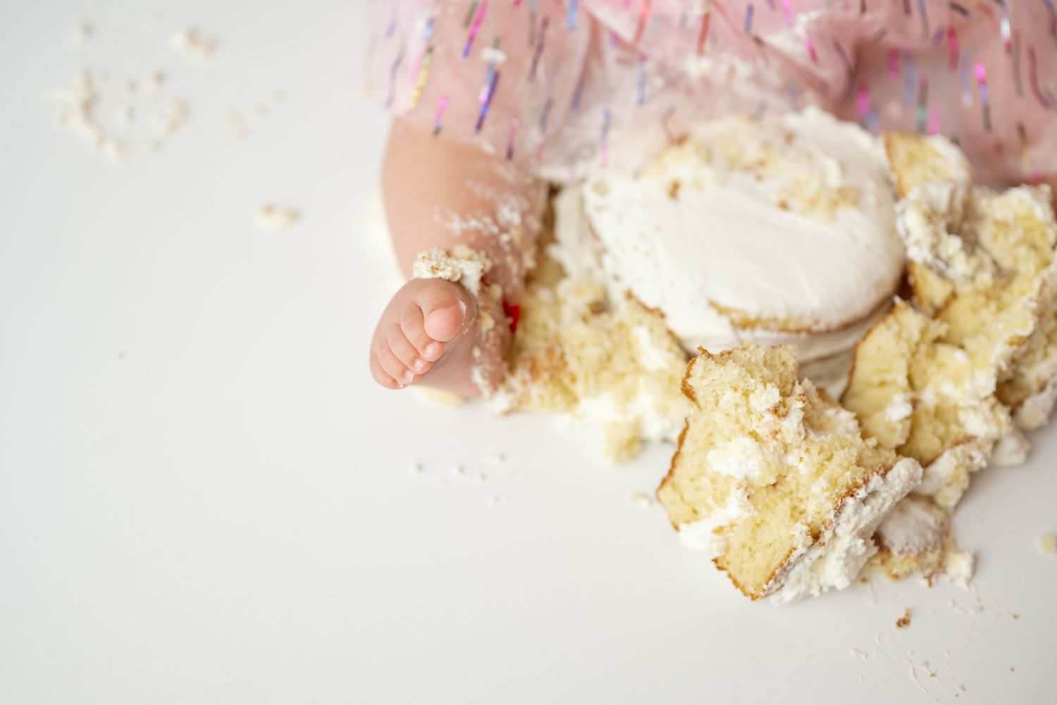 Small hands reach for crumbled vanilla cake with white frosting on a light background.