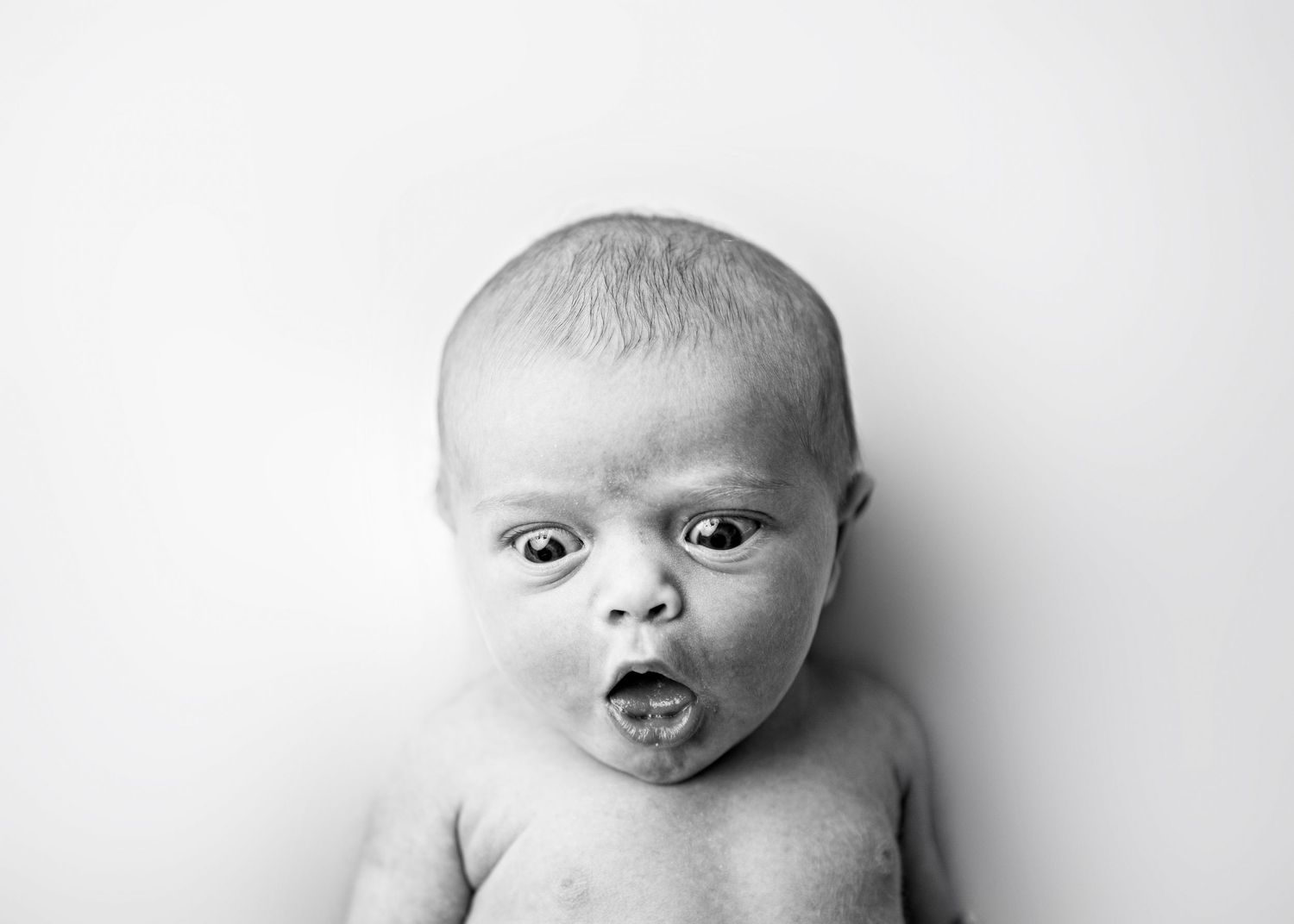 Black and white portrait series showing four close-up expressions of a baby in dramatic lighting.