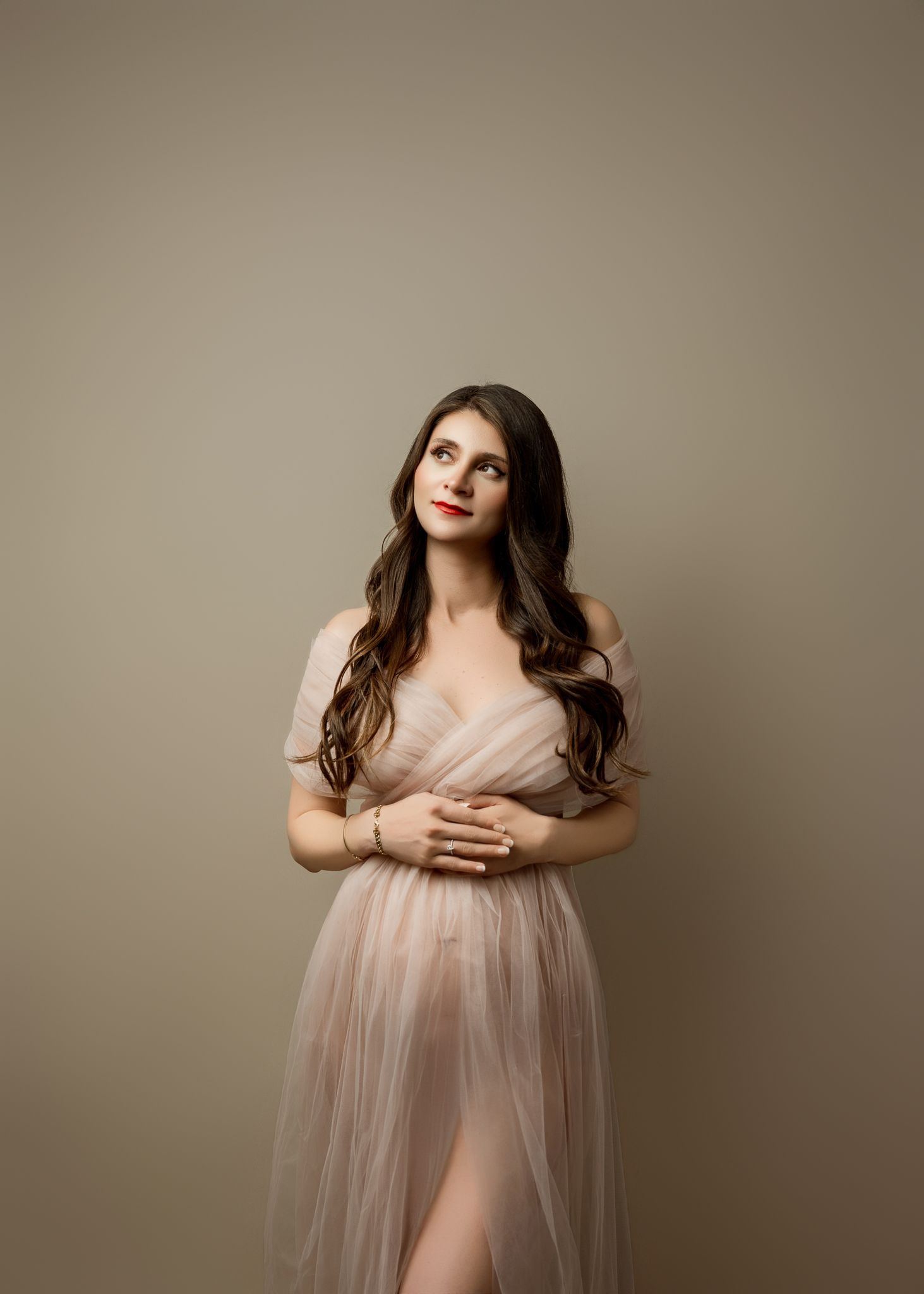 Studio portrait in soft beige tones featuring a romantic tulle gown with off-shoulder design and flowing fabric.