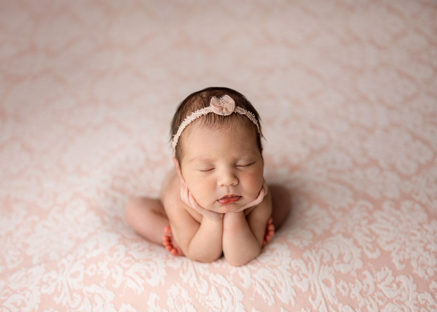 A sleeping newborn baby rests peacefully on soft pink blankets in a professional photography session.