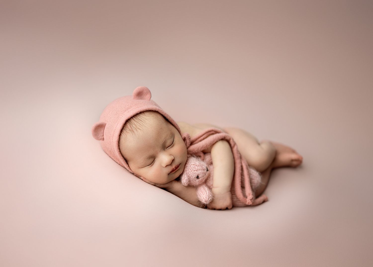 A series of minimalist newborn baby portraits on soft pink backgrounds showing peaceful sleeping poses.