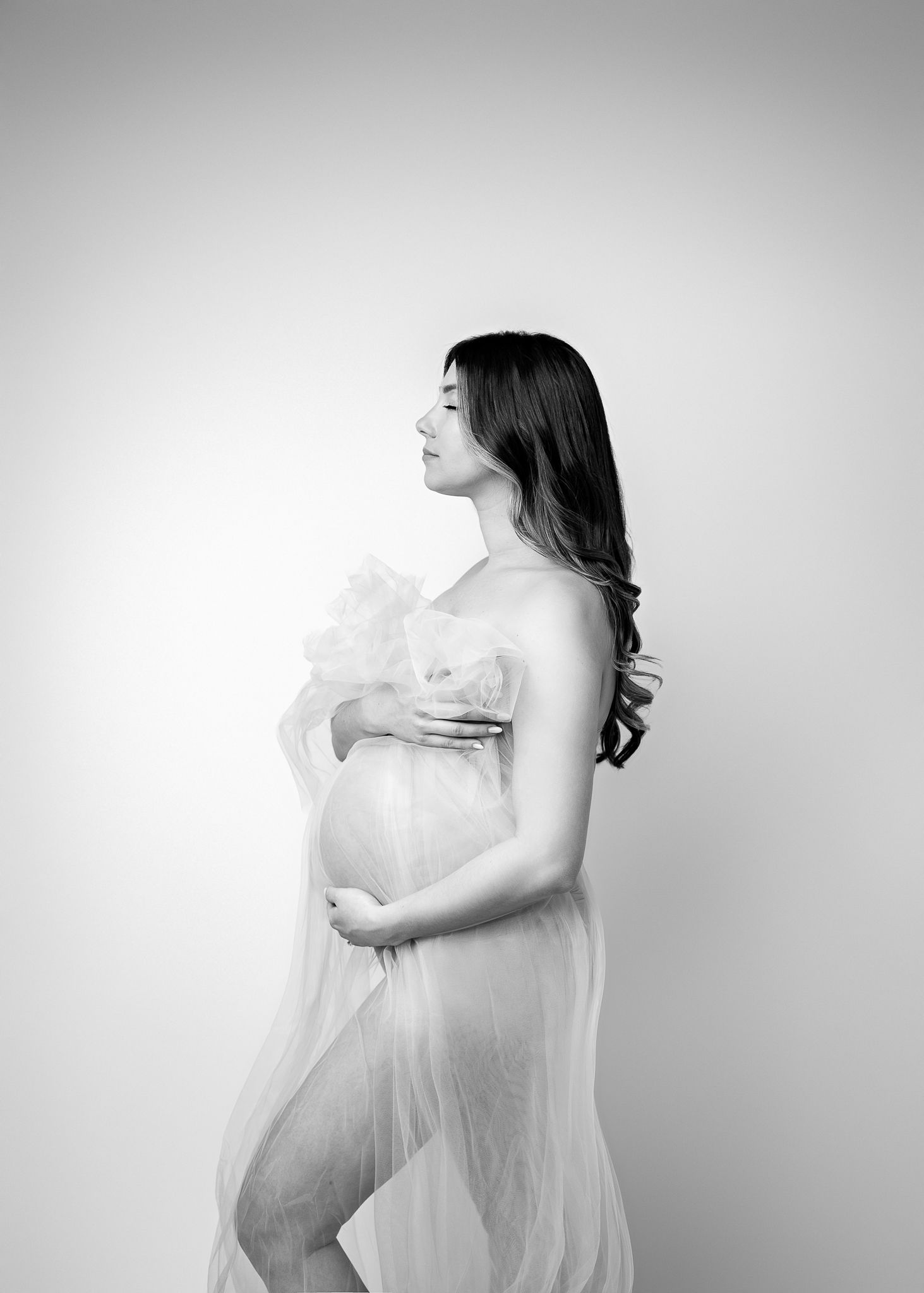 Artistic black and white maternity photo of an expectant mother in flowing sheer fabric.