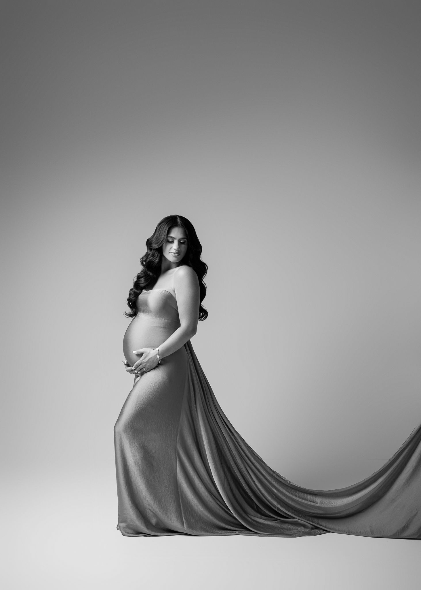 Elegant black and white maternity portrait showing a flowing dress with long train against a simple studio backdrop.