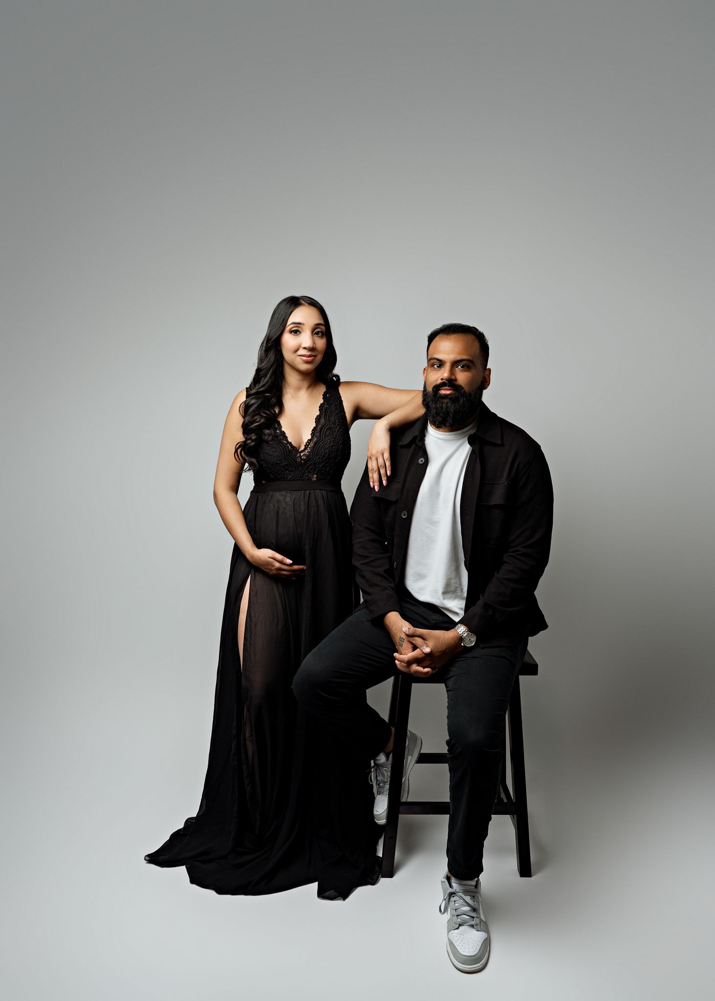 A couple in coordinated black and white outfits pose together in a minimalist studio setting for maternity photos.