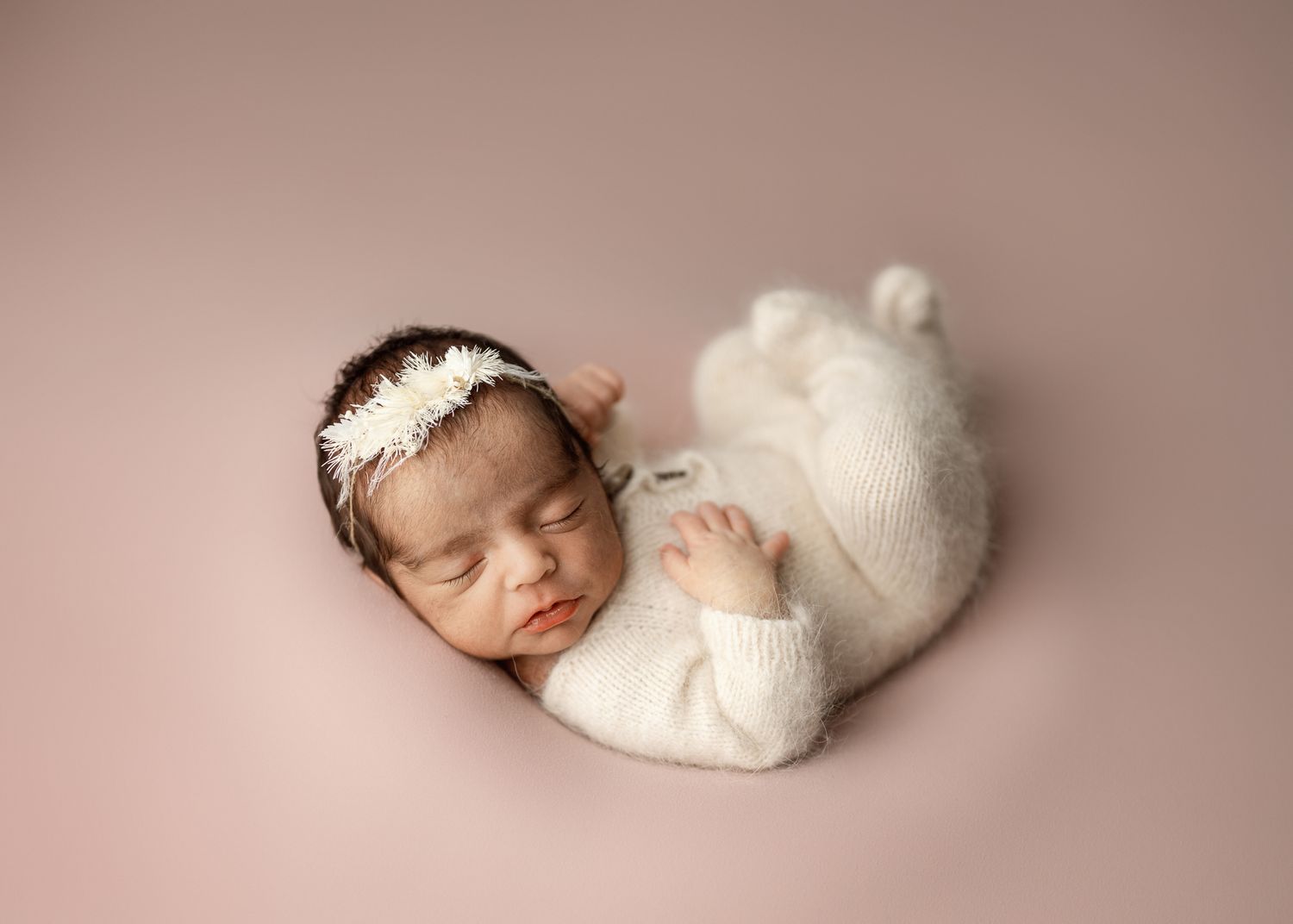 Newborn baby sleeping peacefully in soft white wrap on pink background in professional studio setting.