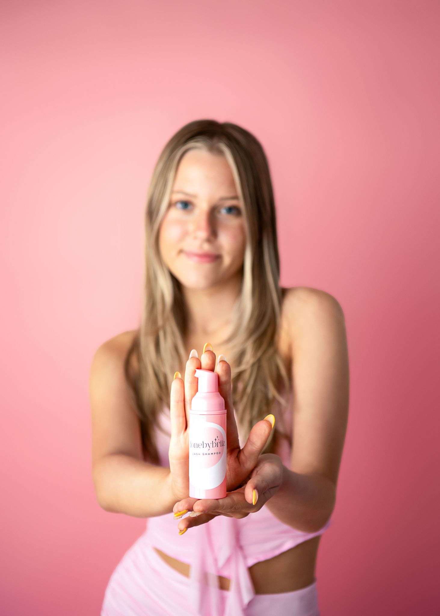 A person in pink clothing holds up a product against a pink backdrop for a lifestyle product photoshoot.