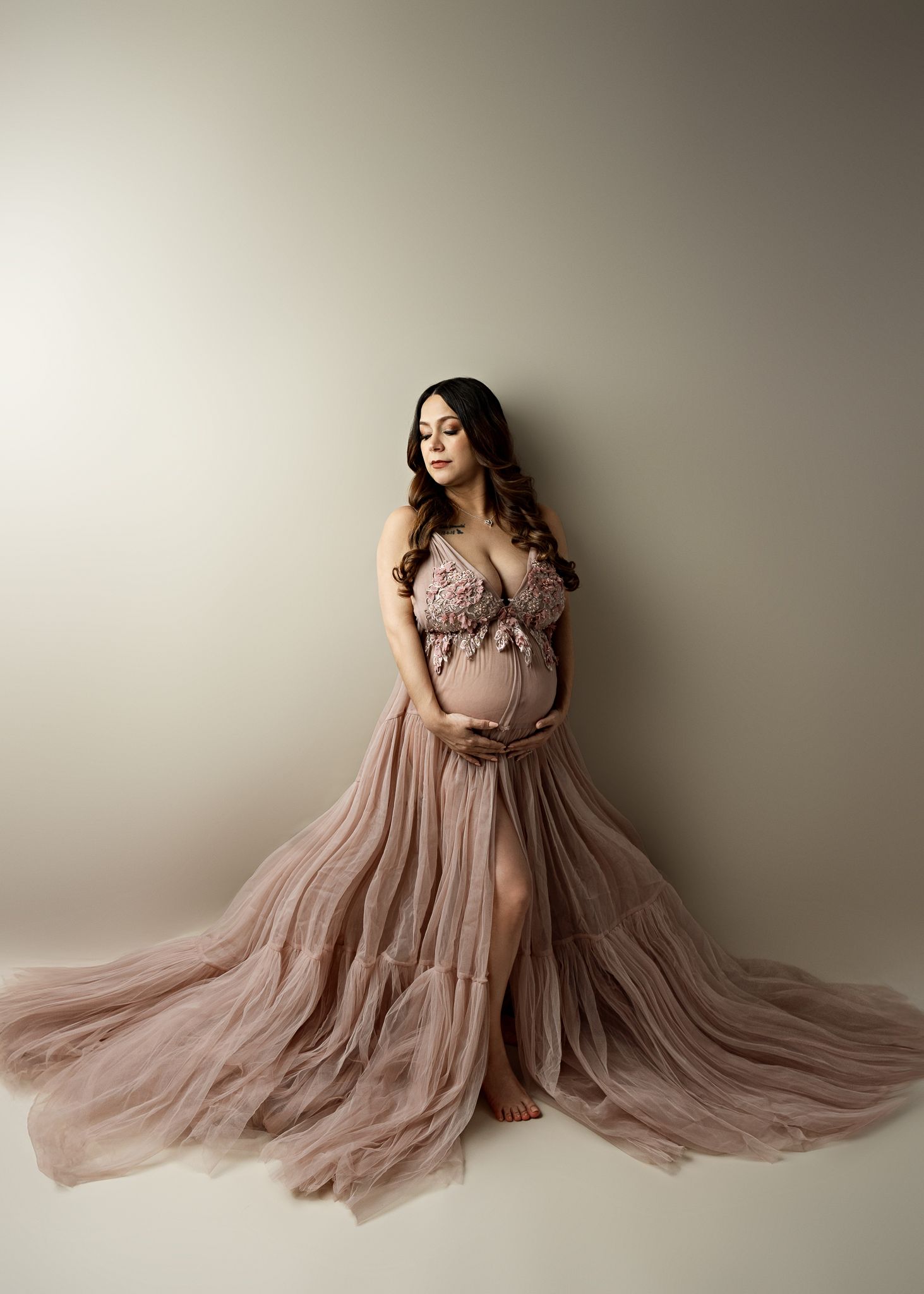 Elegant maternity portrait in flowy mauve tulle gown against neutral backdrop with dramatic flowing train.