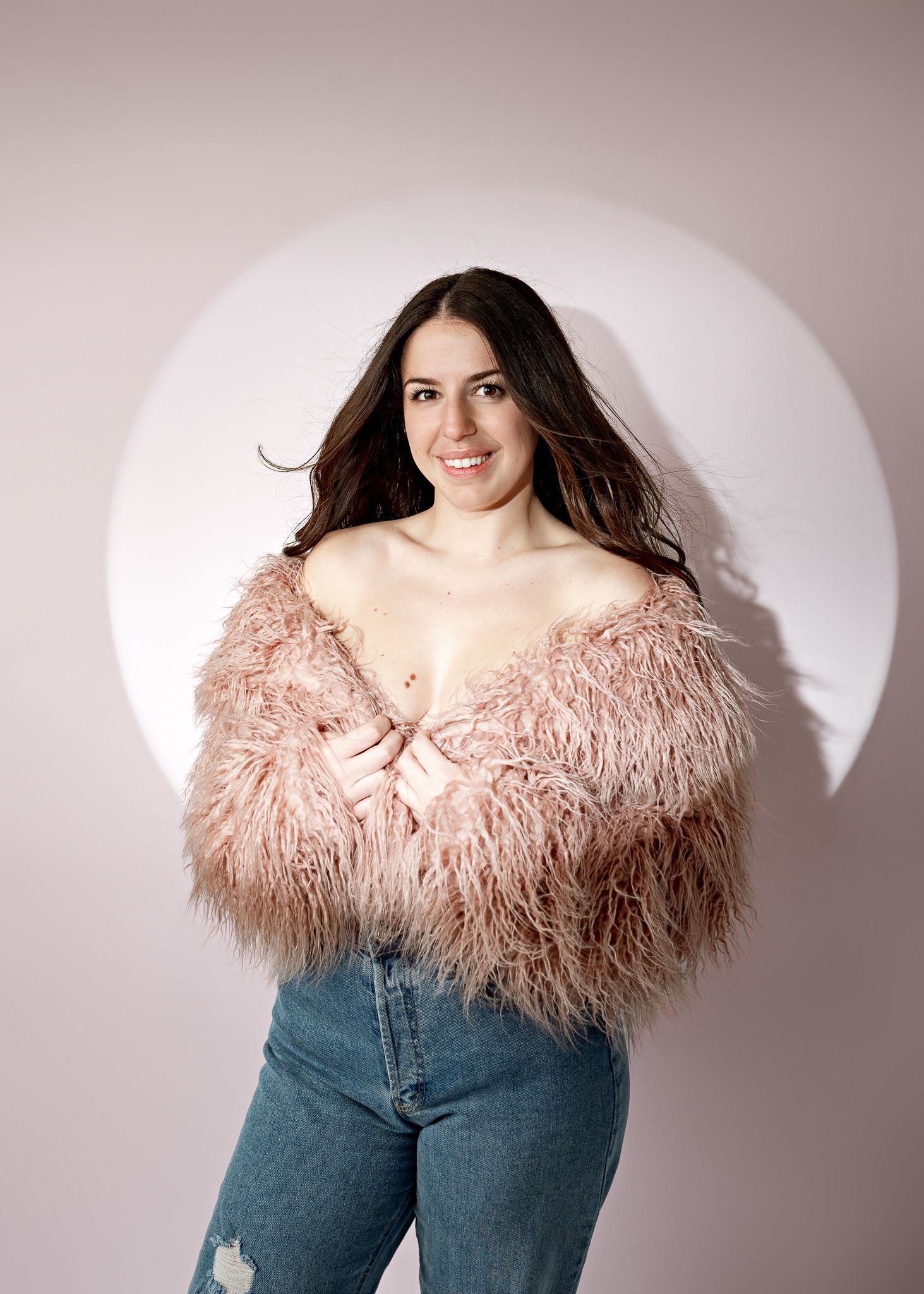 Model wearing pink feathered top with blue jeans posing against white background in fashion photoshoot sequence.