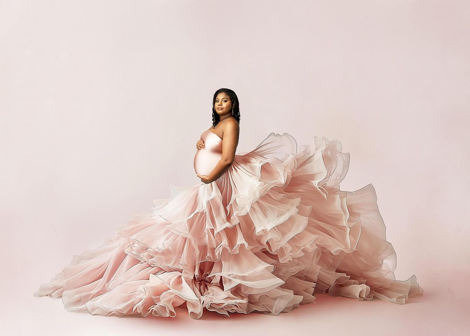 A graceful figure in an elegant blush pink tulle gown with cascading ruffles poses against a soft pink backdrop.