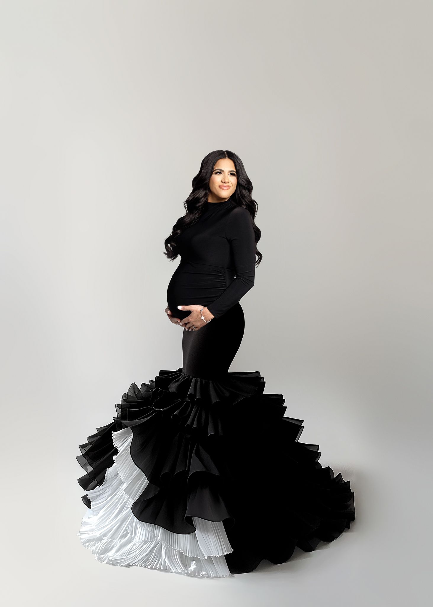 Dramatic black and white maternity gown with layered ruffled mermaid skirt photographed against a grey studio background.
