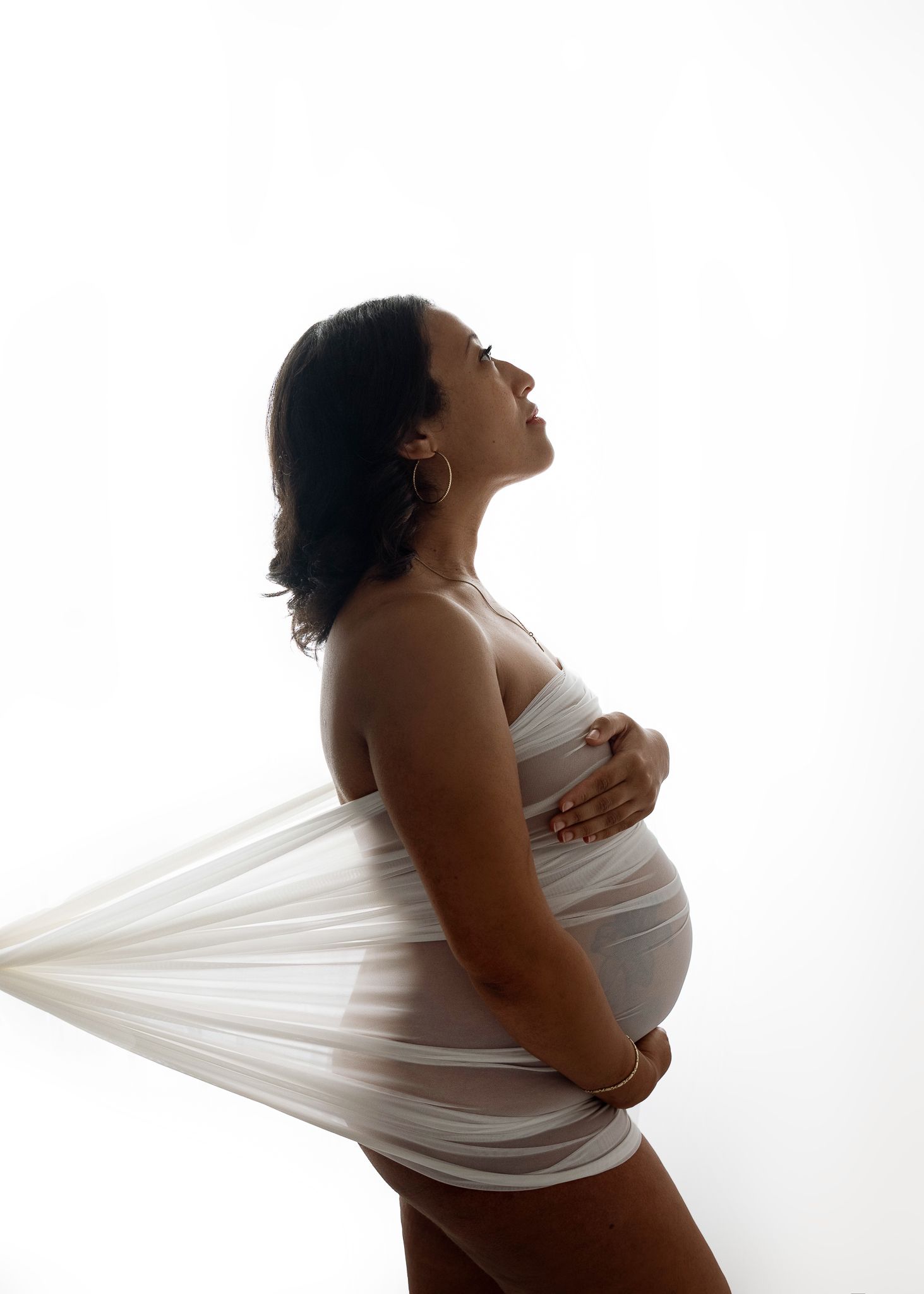 Dramatic side profile silhouette of an expectant mother in white fabric against bright background.