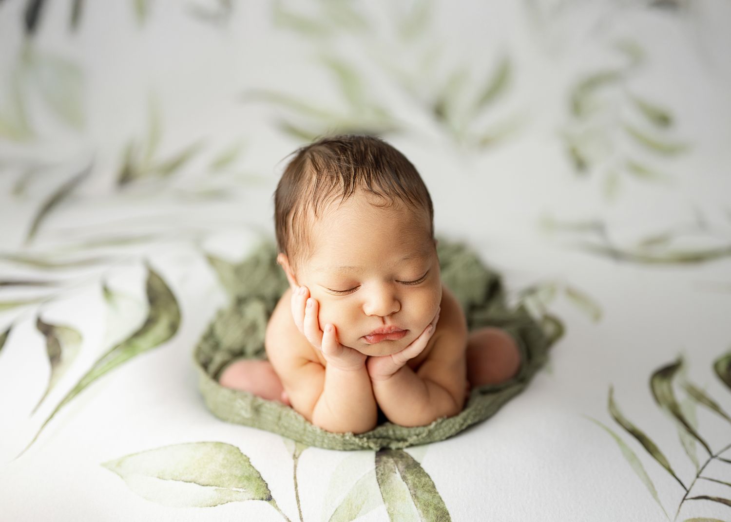 Sleeping newborn lies on soft mint green blanket in minimalist white setting with floral patterned backdrop.