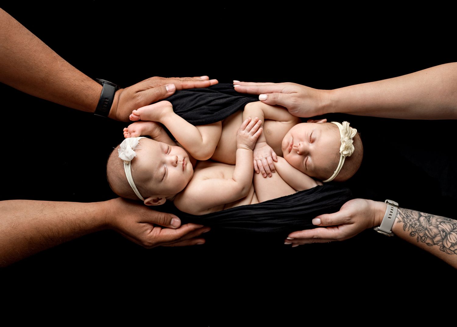 Hands tenderly supporting a sleeping newborn baby against a black background in a studio setting.