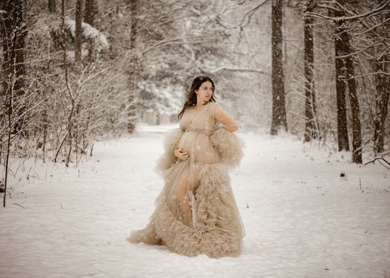 Ethereal cream-colored tulle gown flows dramatically in a snowy winter forest setting.