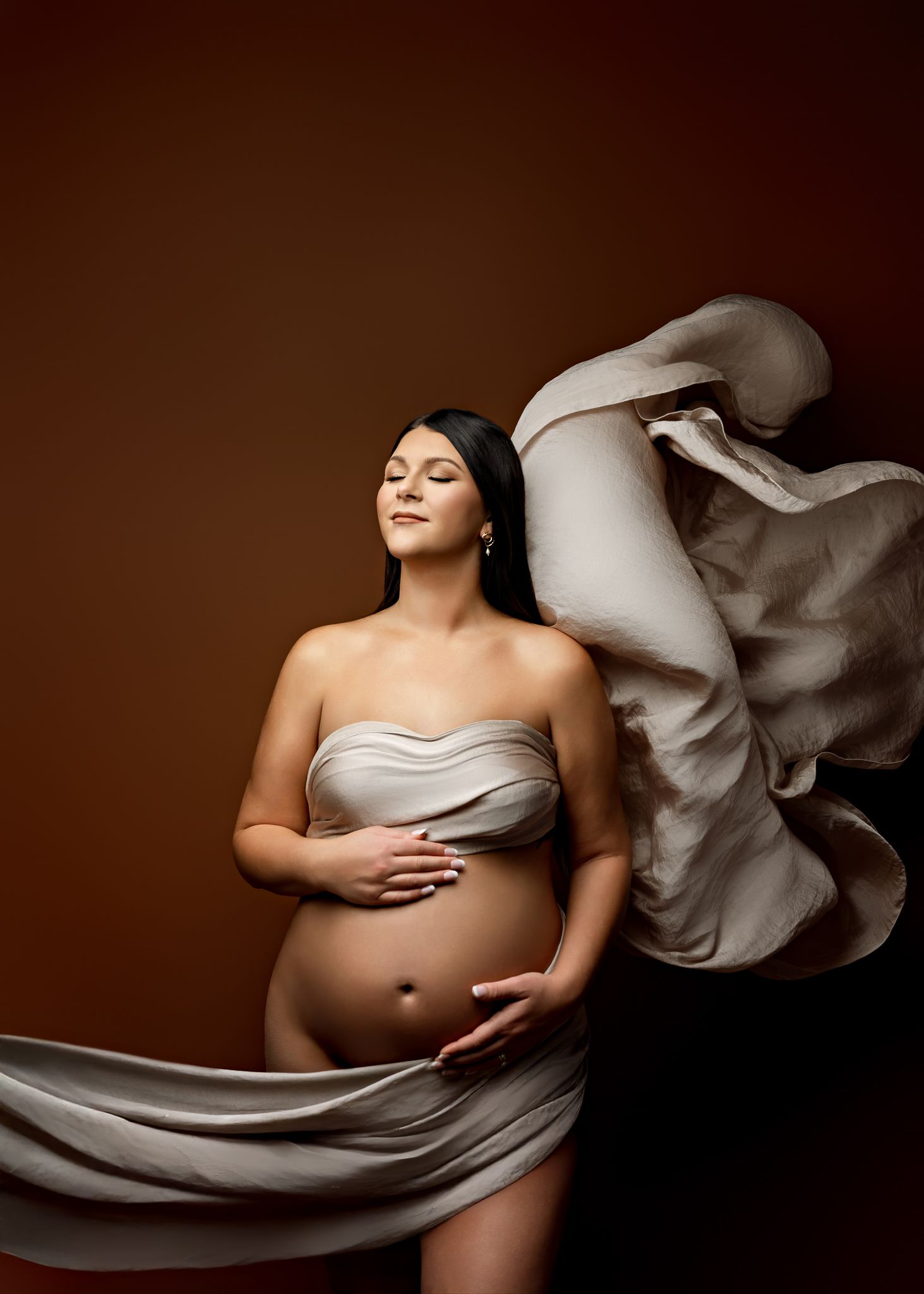 Artistic maternity photo series showing a pregnant woman draped in flowing white fabric against a dark background.